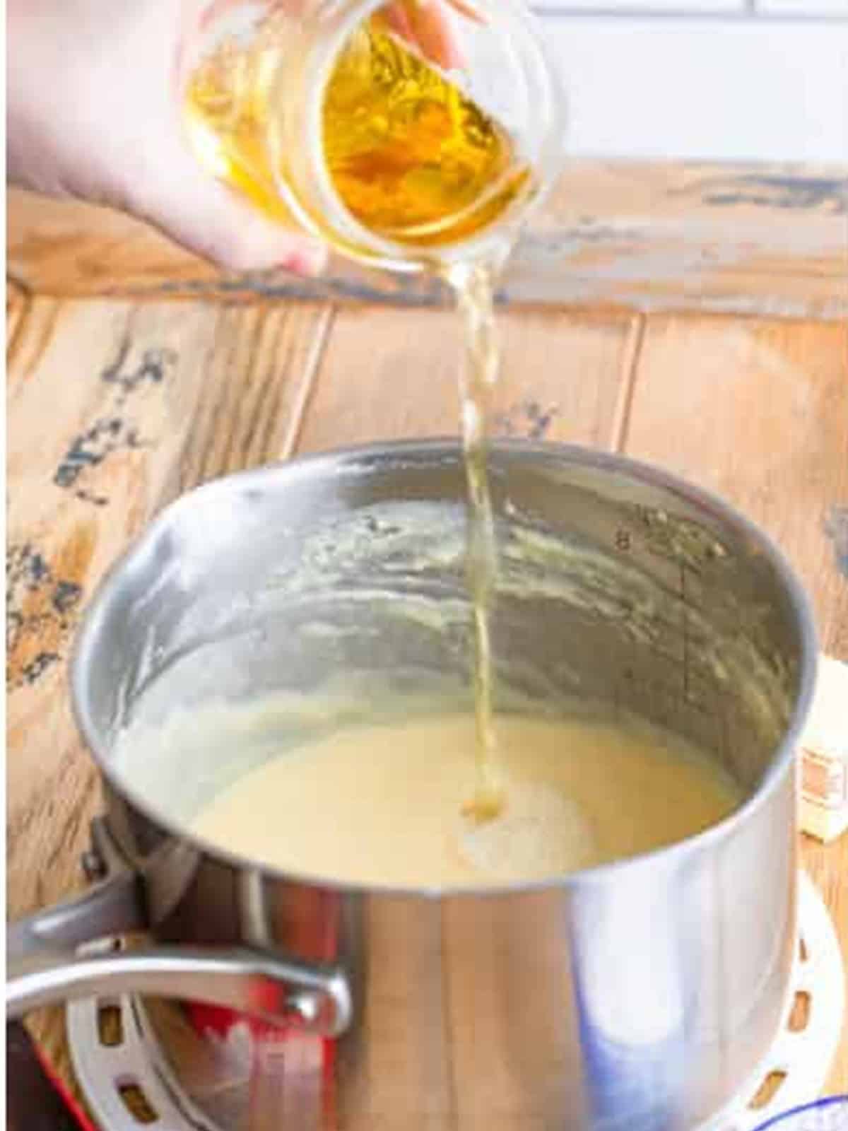 Beer being poured into the creamy base in a saucepan for beer cheese dip.
