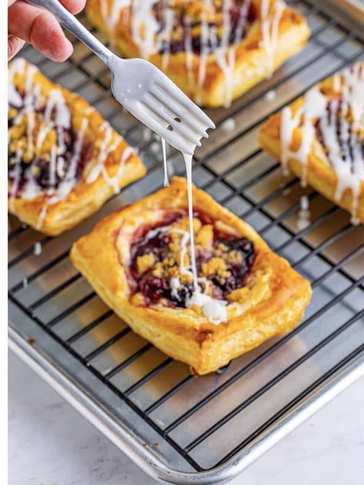 Glaze drizzled over the baked berry danish on a cooling rack.