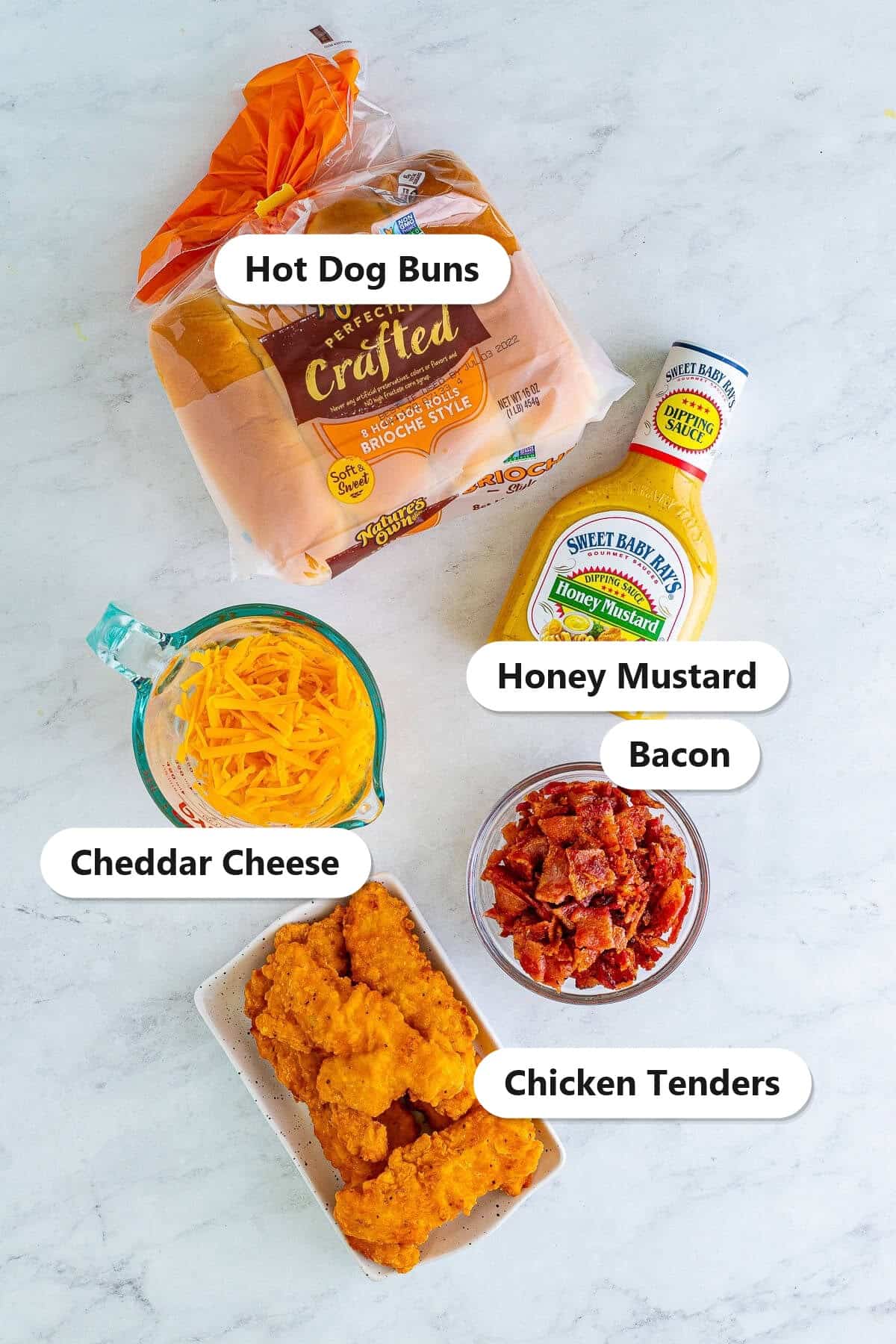 Labeled ingredients to make a bird dog sandwich including hot dog buns, honey mustard, cheddar cheese, bacon, and breaded chicken tenders.