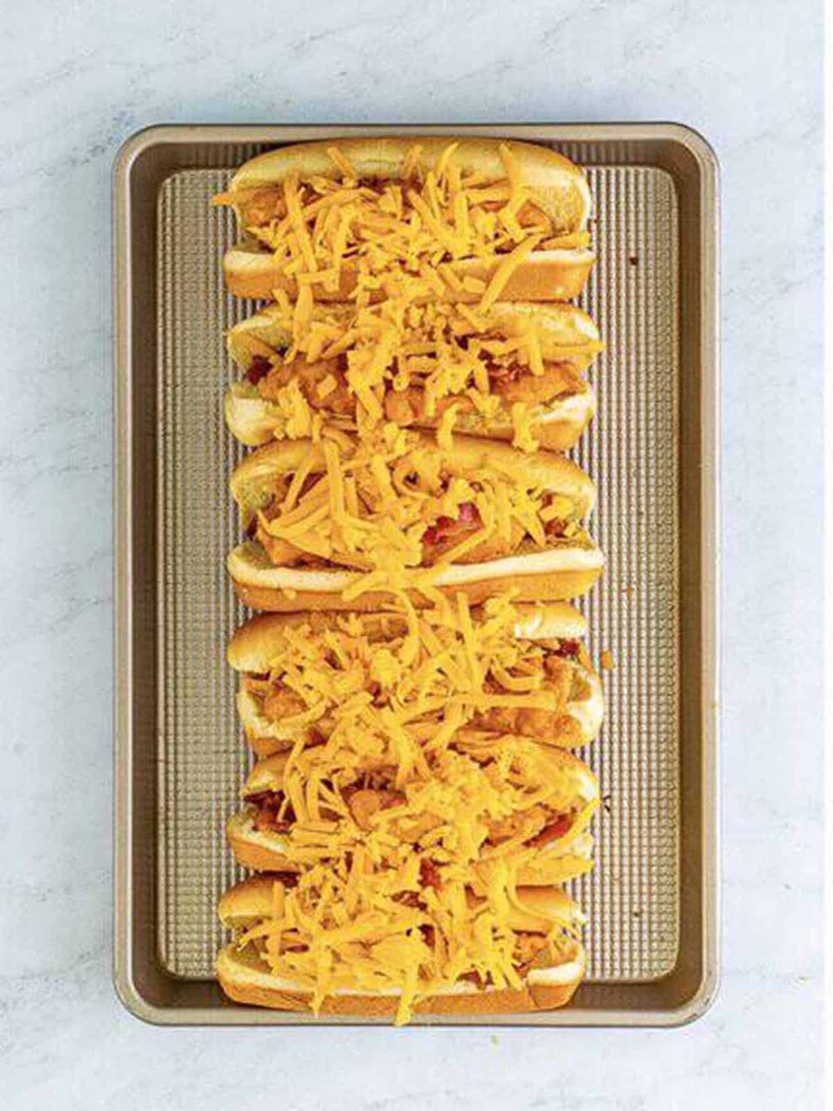 A full tray of bird dog sandwiches topped with shredded cheddar ready to bake.