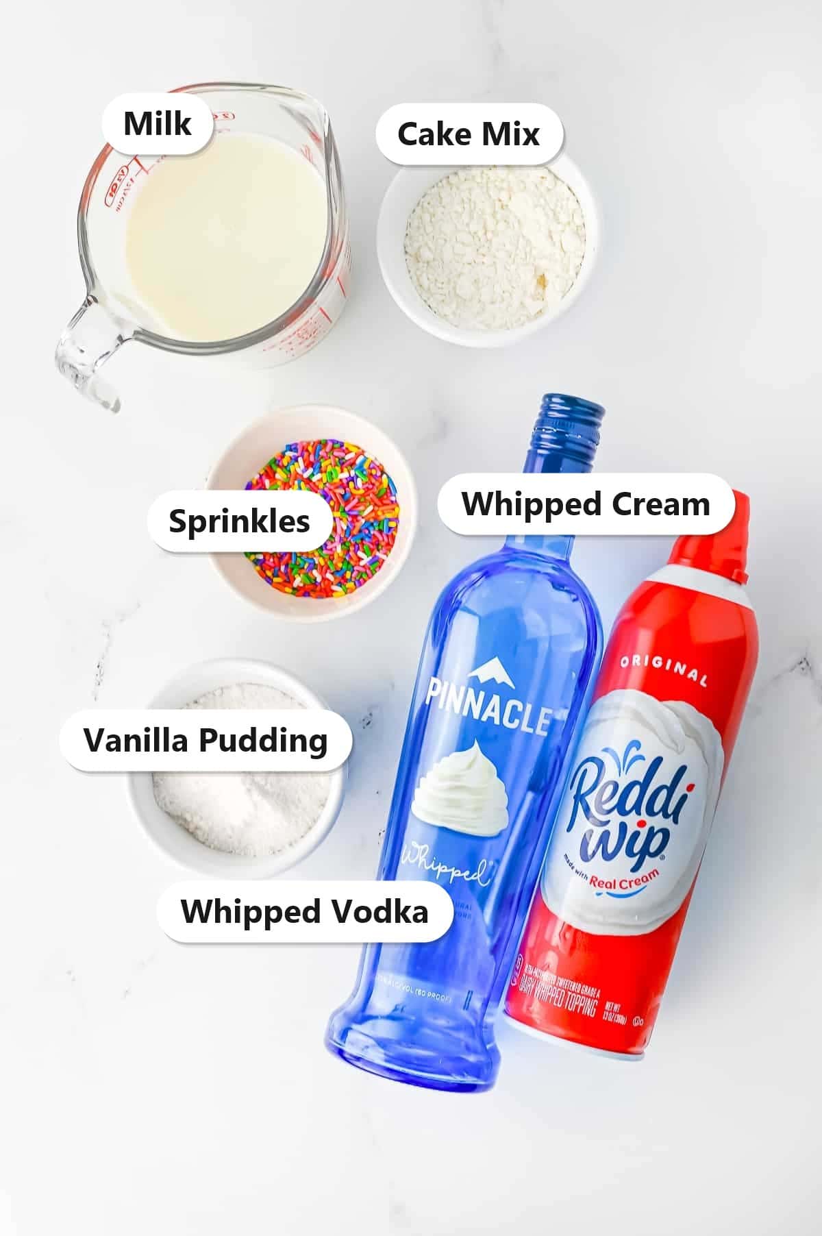 Labeled ingredients to make birthday cake pudding shots including vanilla pudding, cake mix, milk, whipped vodka, whipped cream, and sprinkles.