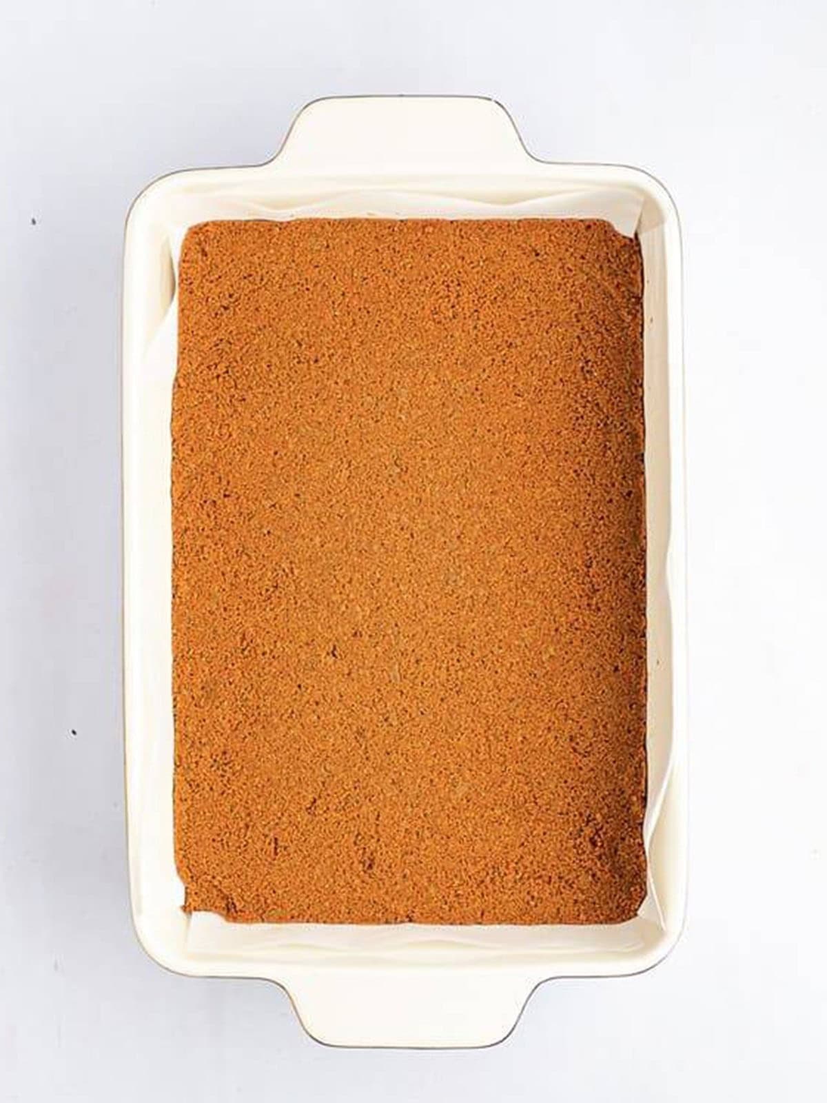 Biscoff cookie crust pressed into a parchment lined baking dish.