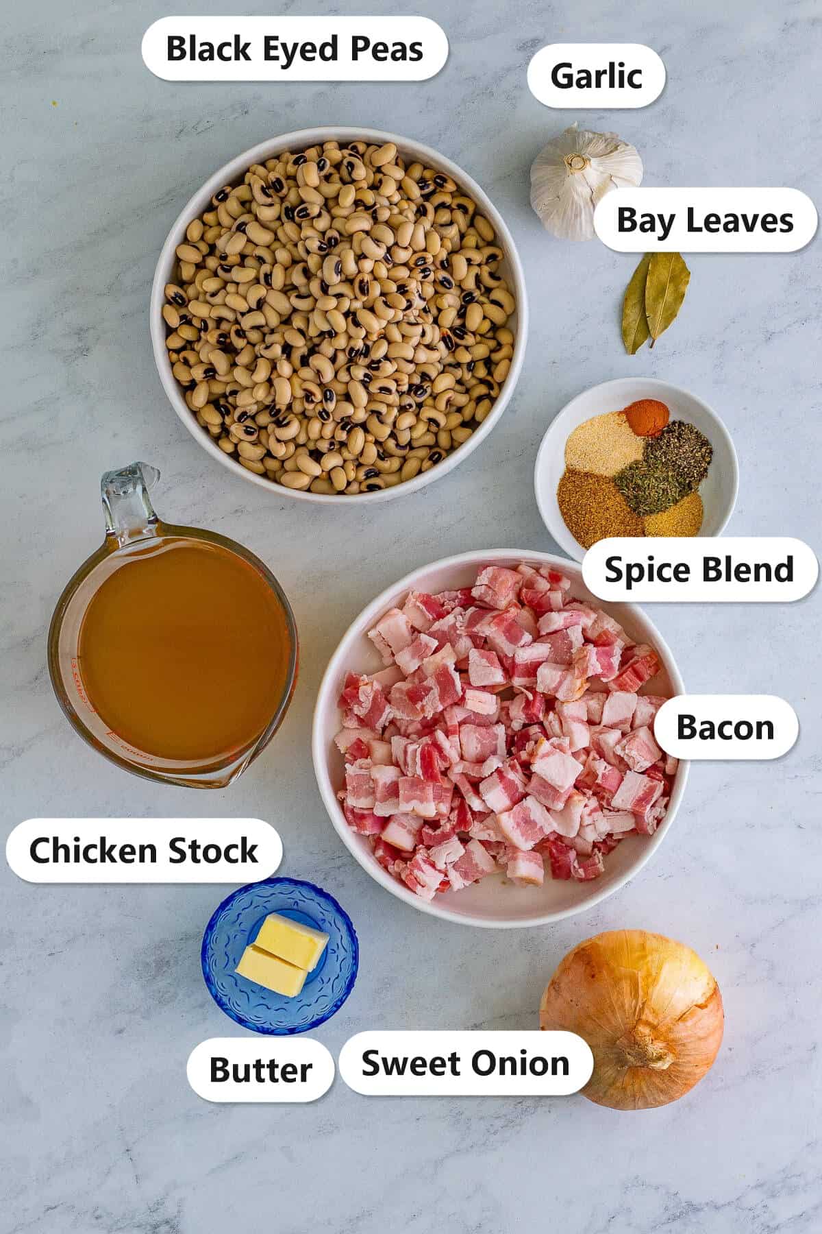 Labeled ingredients for black eyed peas recipe including dried black eyed peas, bacon, chicken stock, spice blend, garlic, bay leaves, butter, and sweet onion.