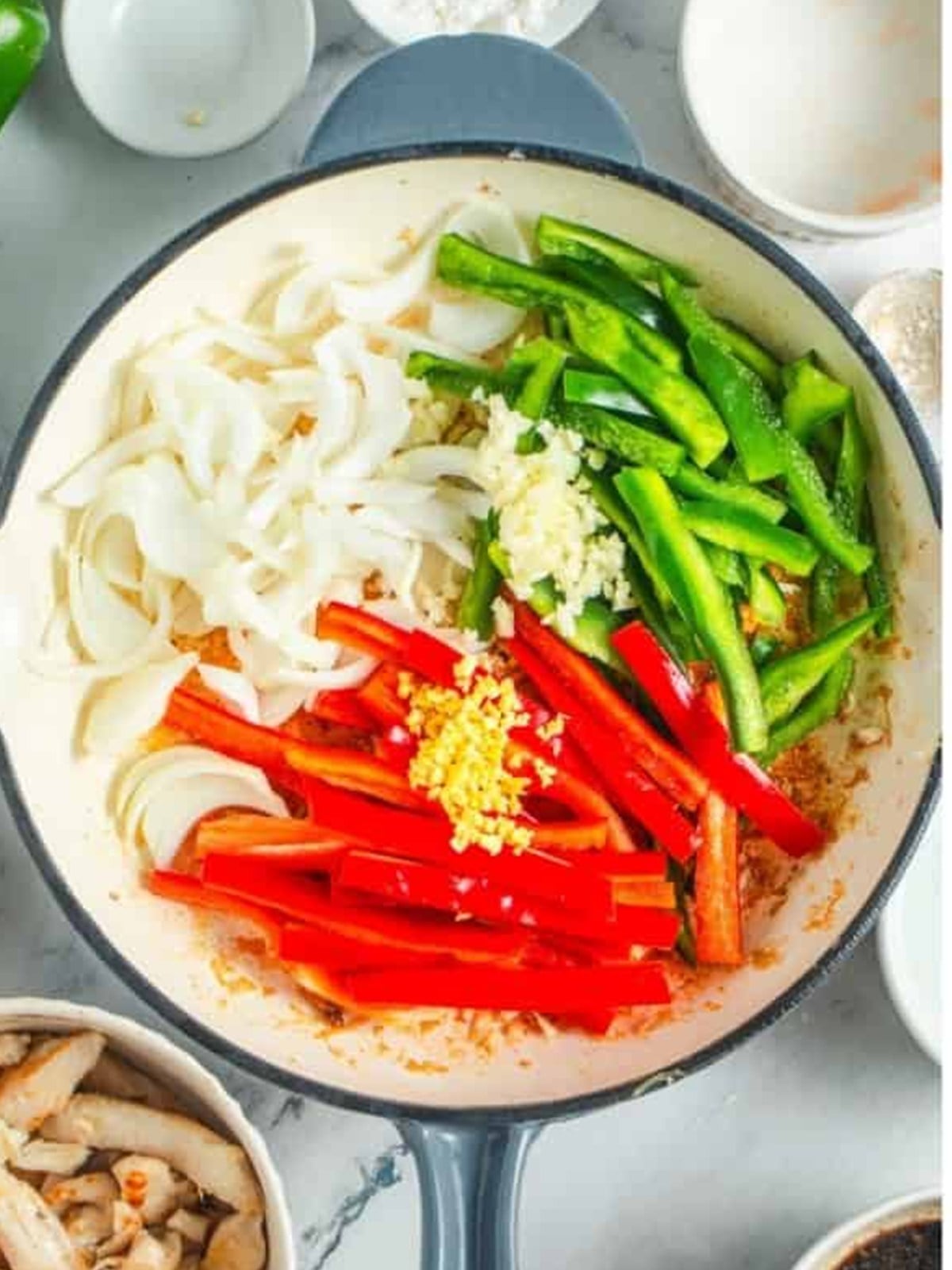 Sliced onion, red and green bell peppers, garlic, and ginger added to a skillet for black pepper chicken.