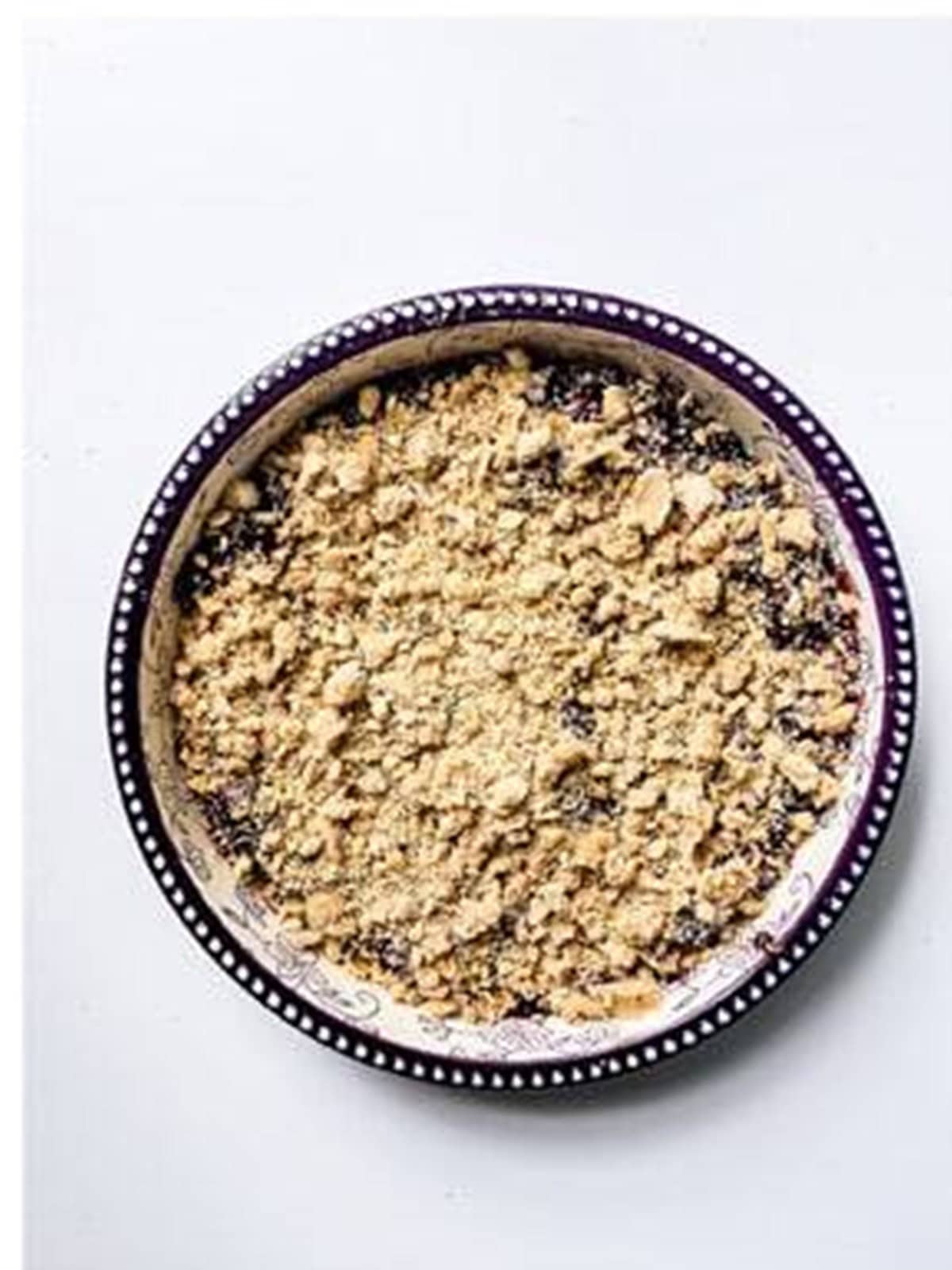 Crumble topping sprinkled over blackberry filling in a baking dish.