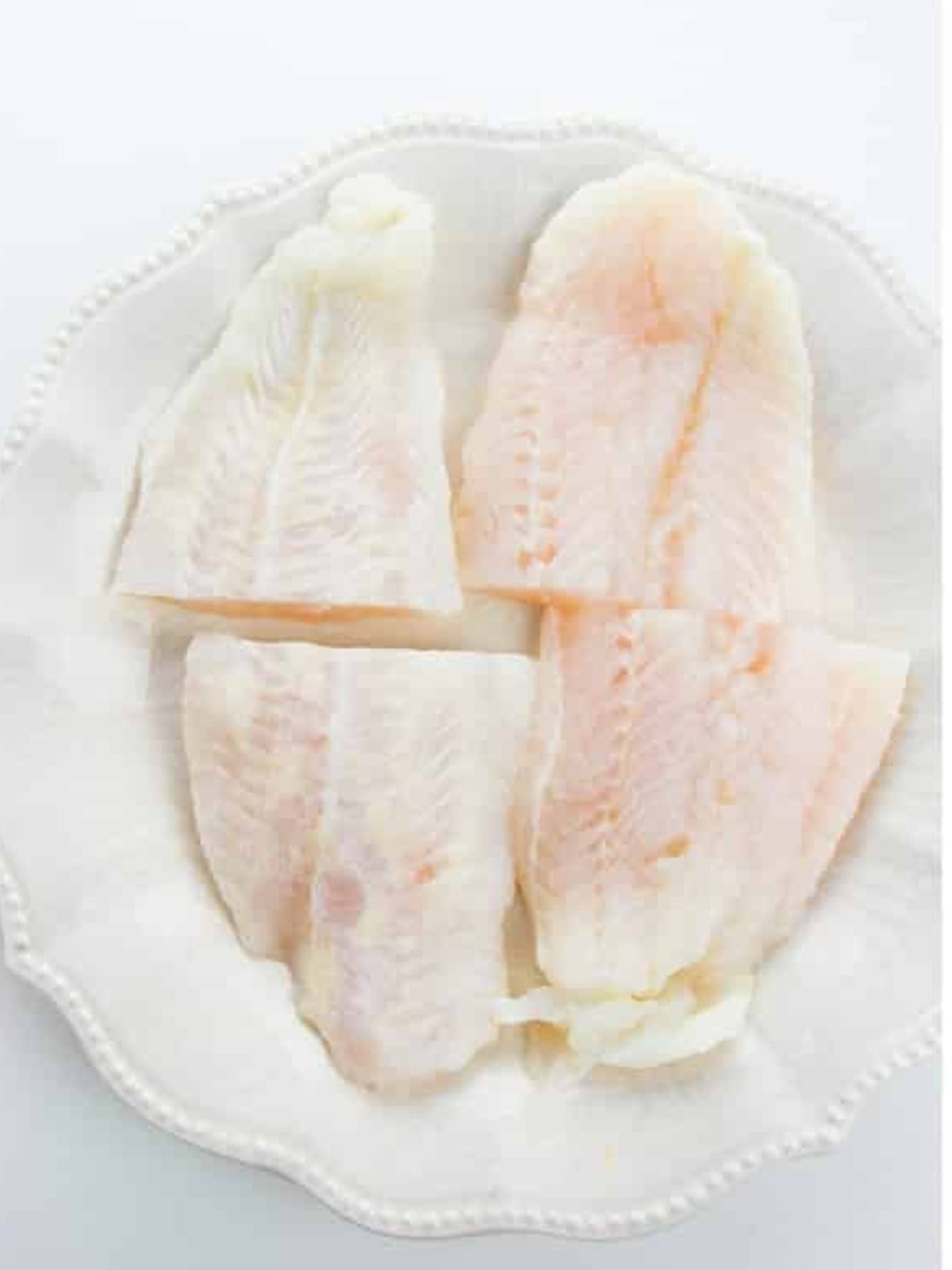Raw catfish filets patted dry on a white plate for blackened catfish.
