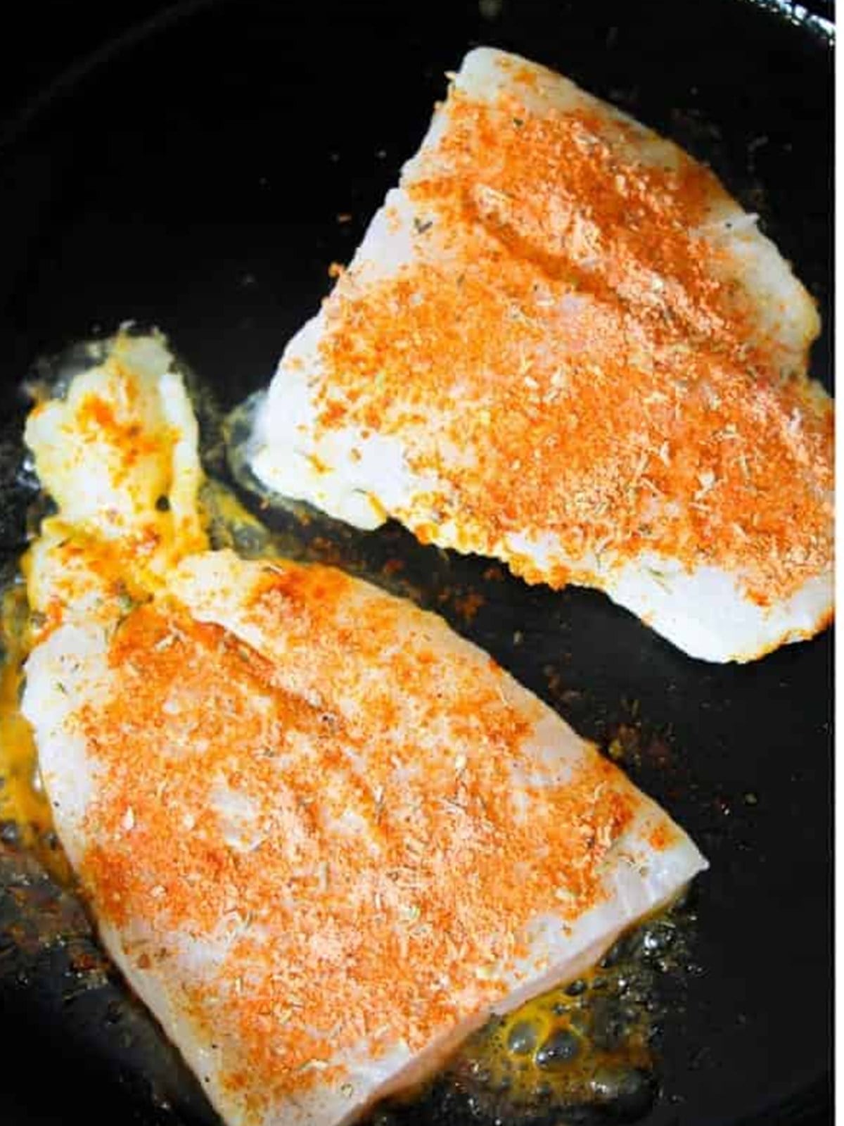 Seasoned catfish filets frying in oil in a hot skillet.