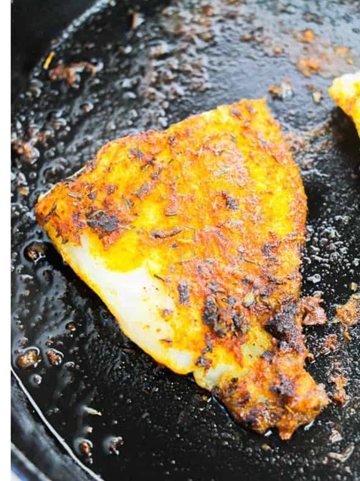 Blackened catfish filet flipped in the skillet, charred and golden.
