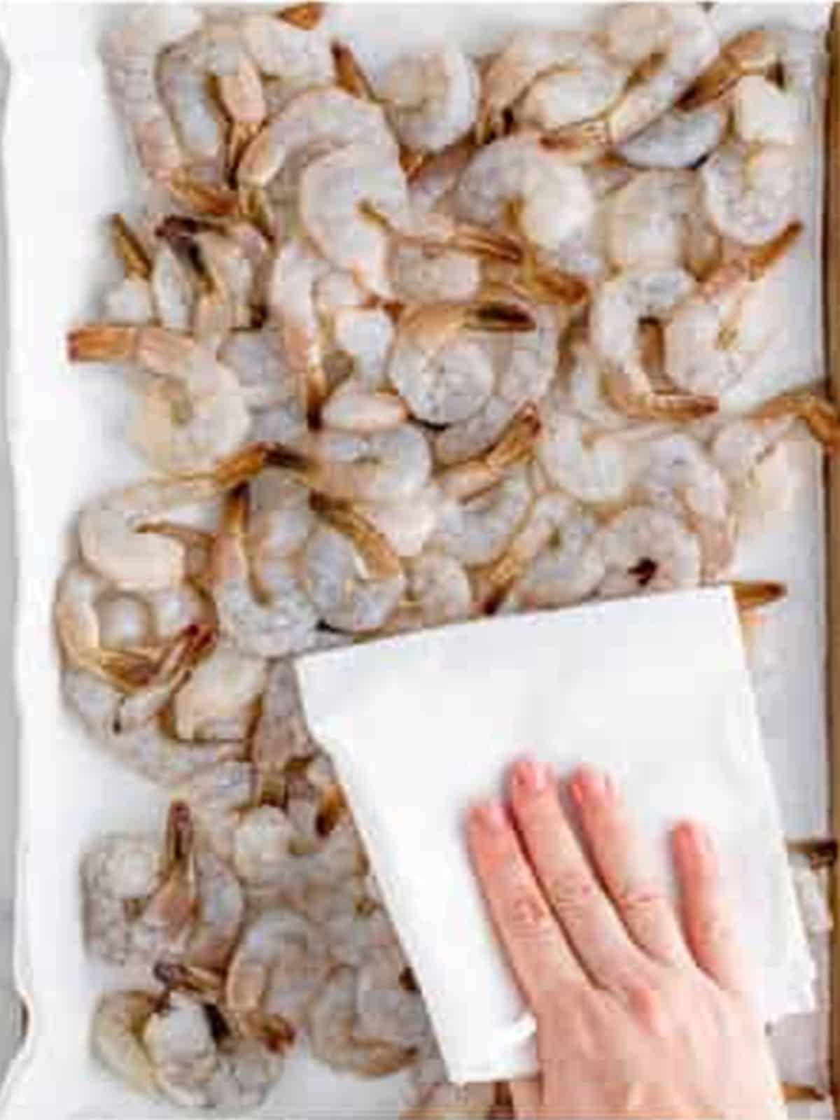 Patting raw shrimp dry with a paper towel on a tray for Blackened Shrimp.
