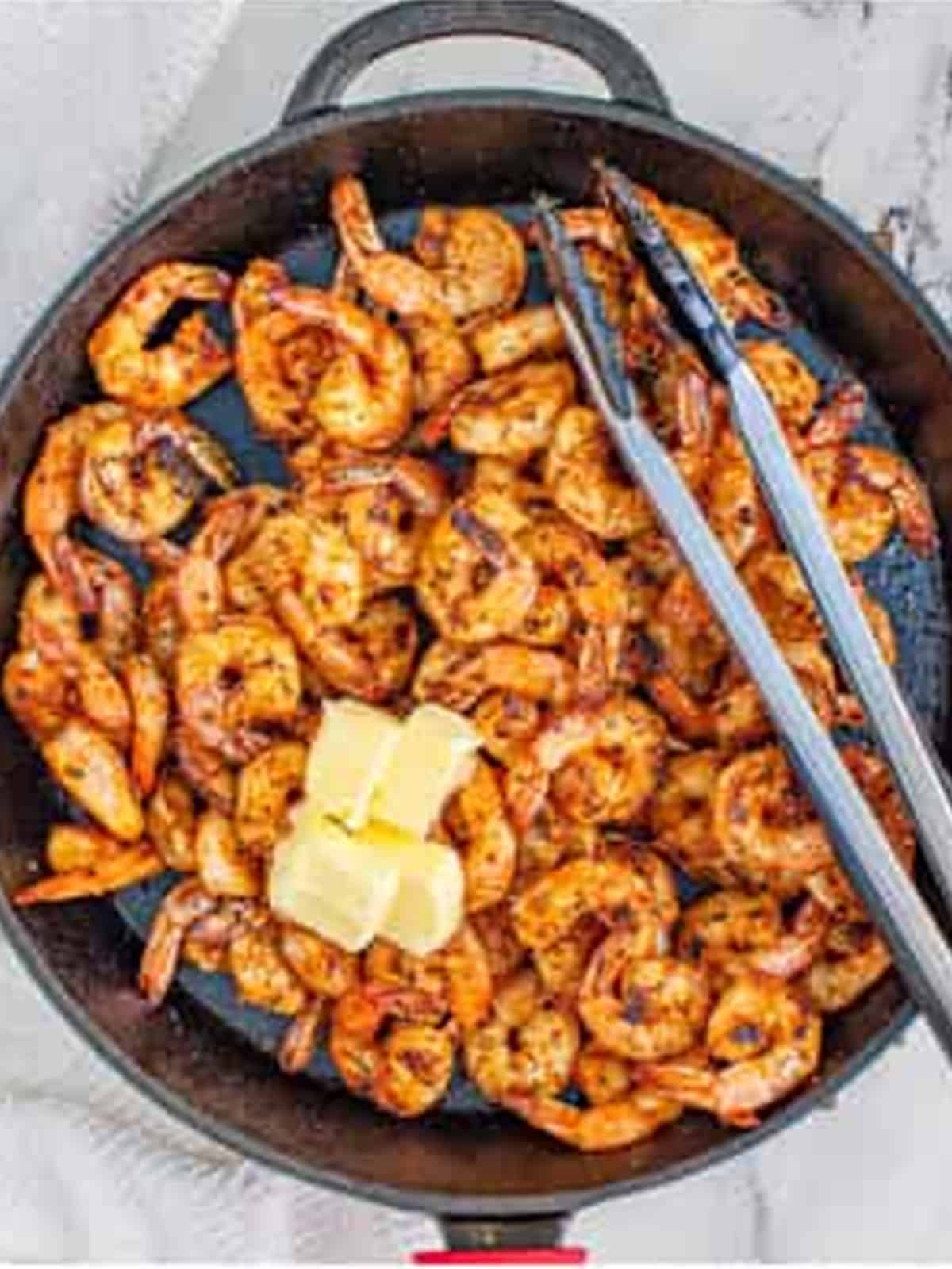 Adding butter to the seared Blackened Shrimp in the cast iron skillet.