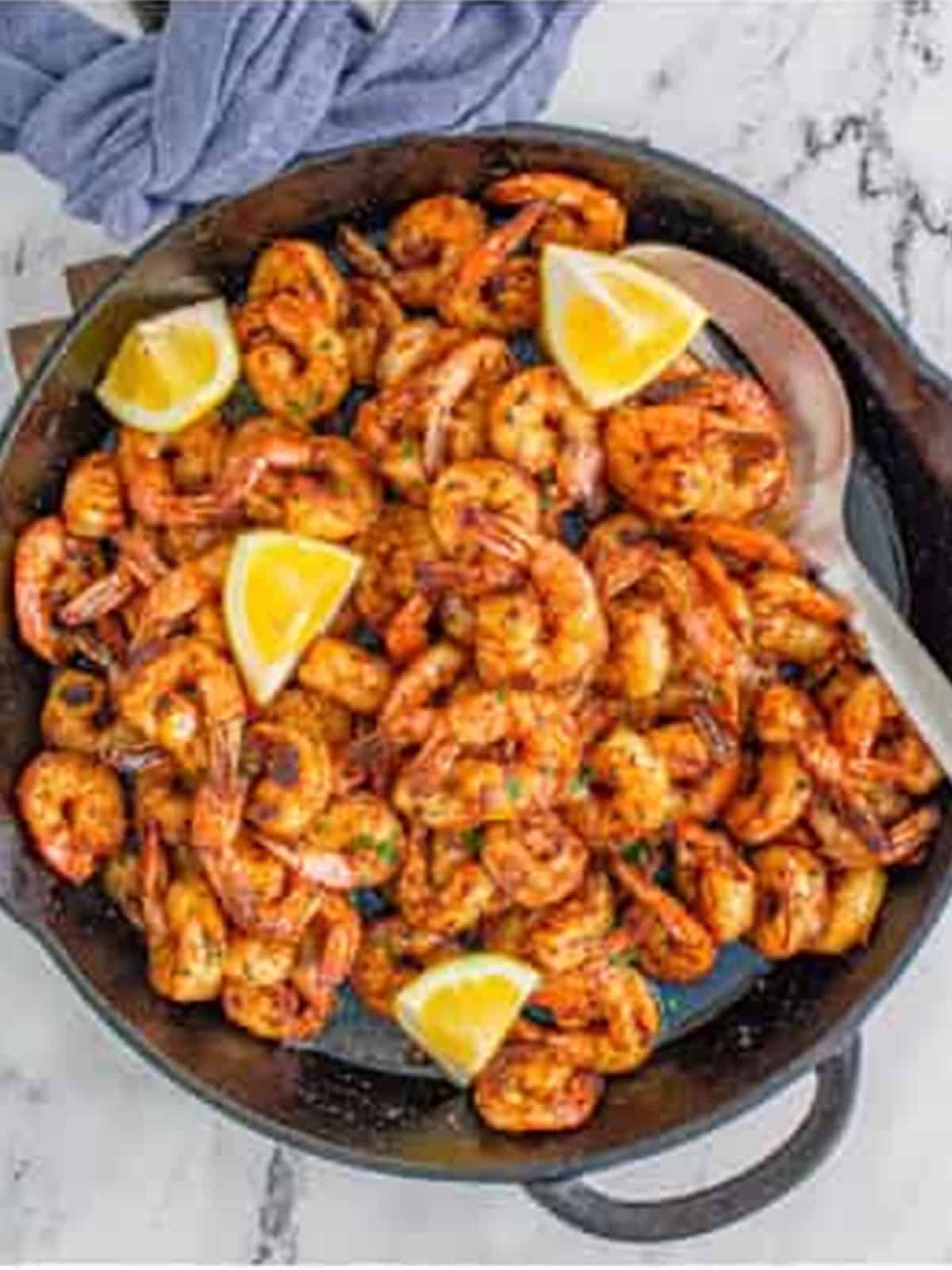 Finished Blackened Shrimp in a skillet garnished with lemon wedges.