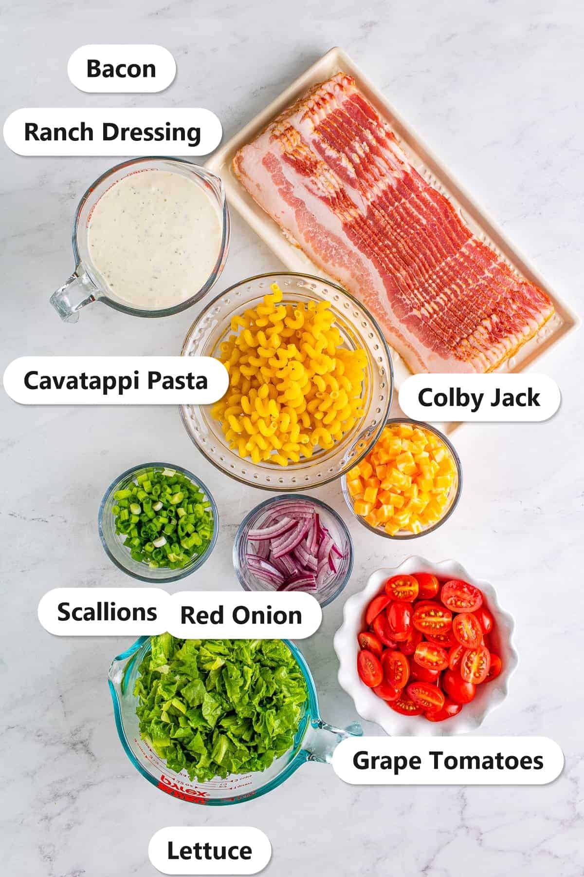 Ingredients to make BLT Pasta Salad laid out and labeled on a marble counter.