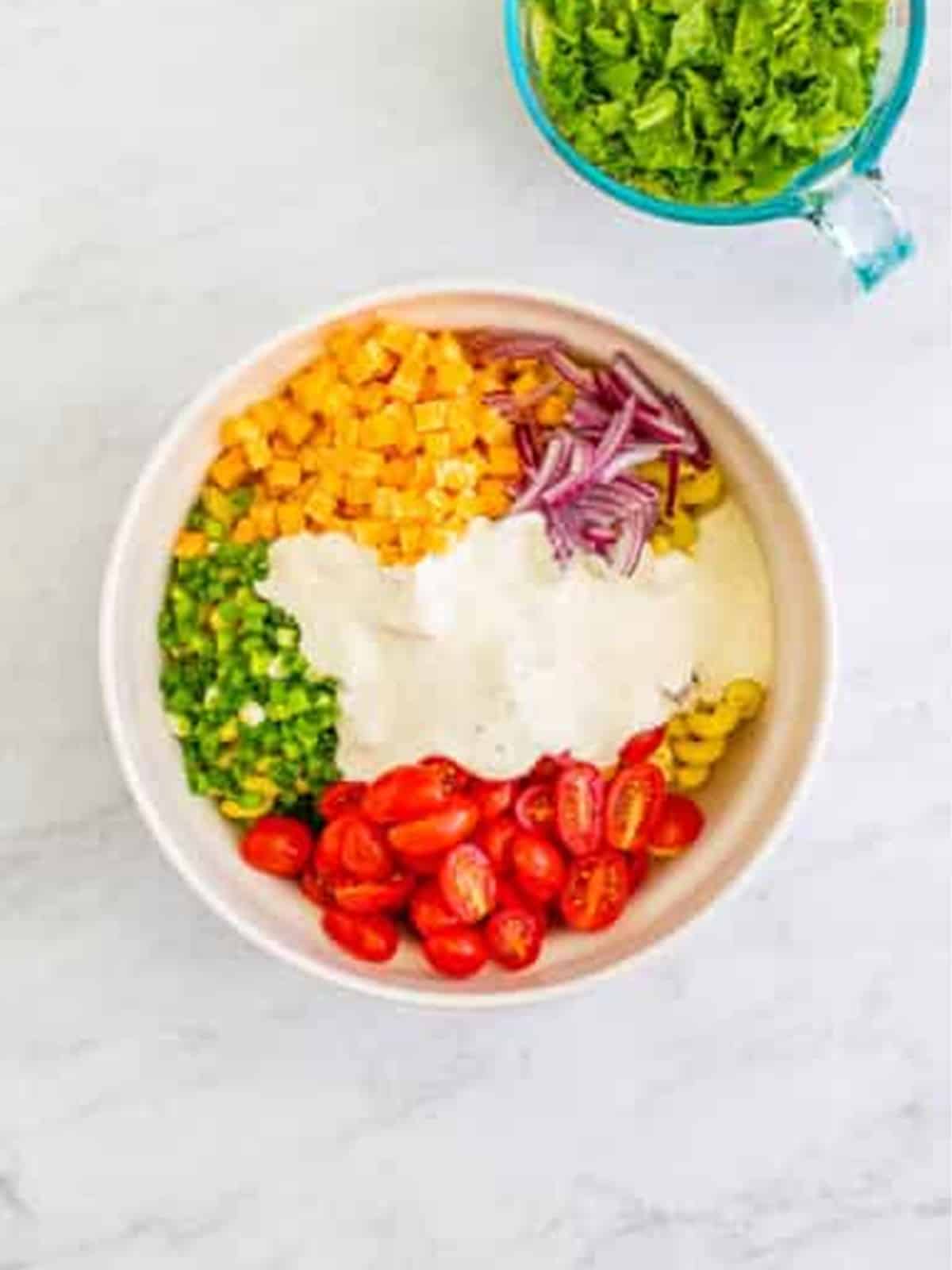 Pasta, Colby Jack, tomatoes, scallions, red onion, and ranch dressing in a bowl for BLT Pasta Salad.