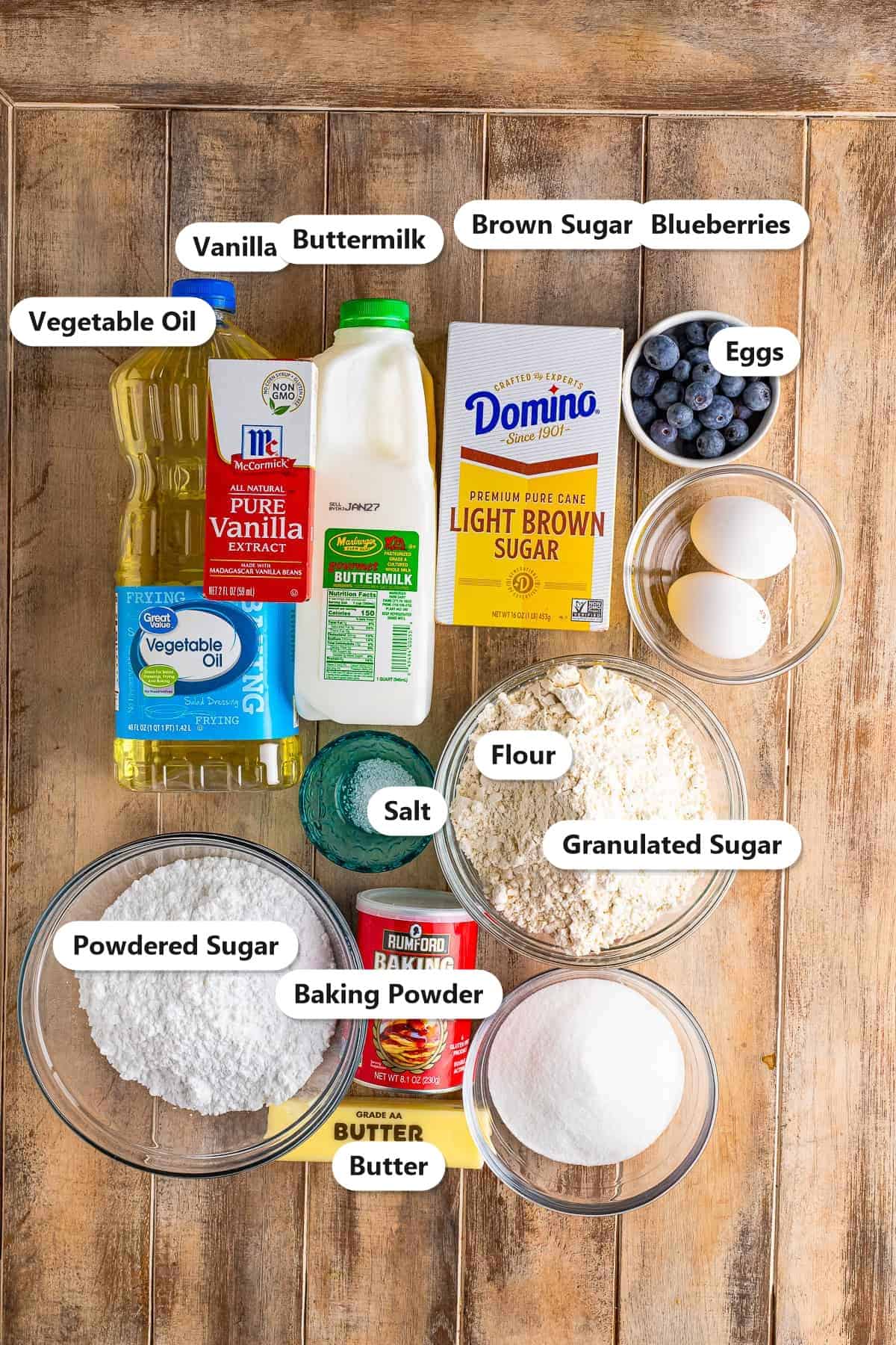 Blueberry Cake ingredients including flour, sugars, buttermilk, oil, eggs, vanilla, blueberries, butter, and powdered sugar labeled on a board.