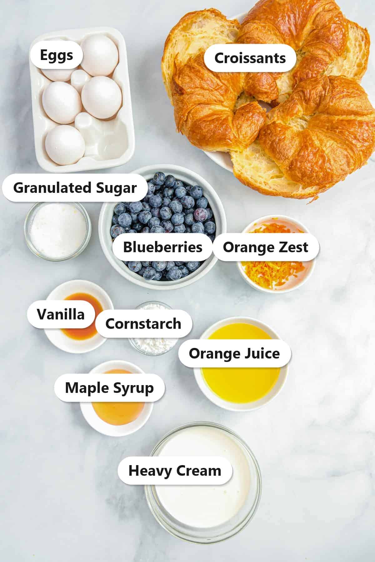 Labeled ingredients to make croissant french toast including croissants, eggs, heavy cream, blueberries, orange juice, orange zest, sugar, cornstarch, vanilla, and maple syrup.