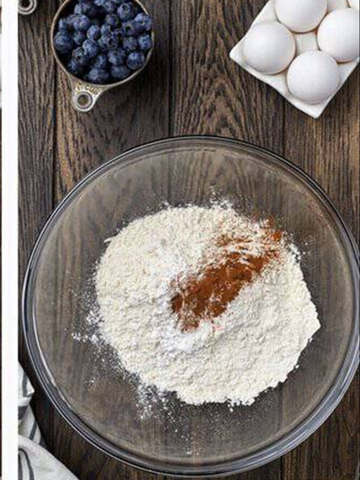 Flour, cinnamon, and leavening whisked together in a bowl for blueberry muffins.