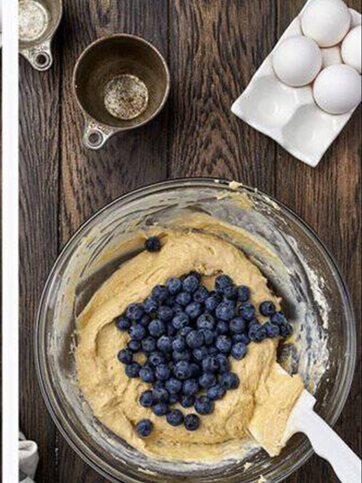 Fresh blueberries being folded into muffin batter with a spatula.