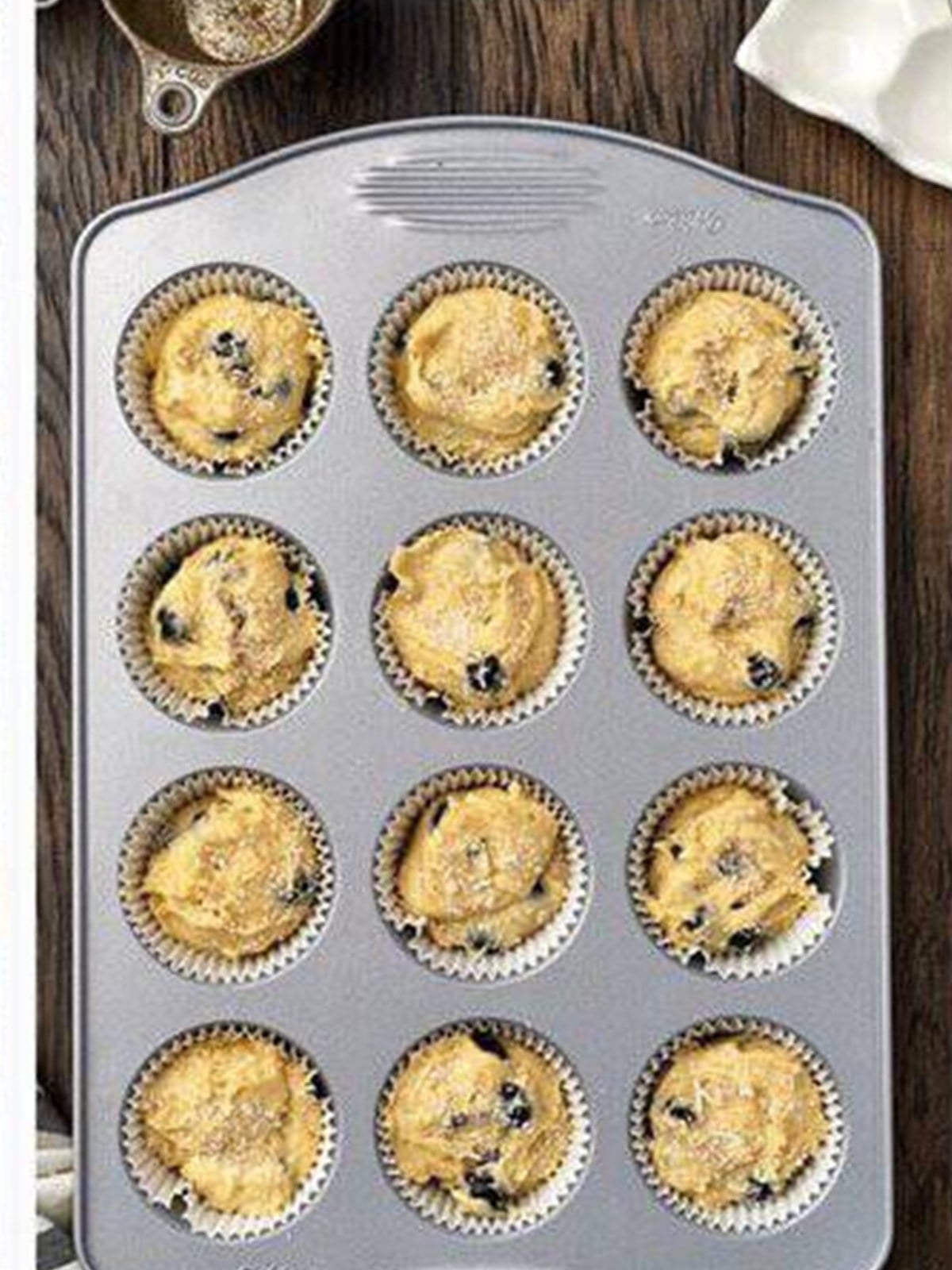 Muffin tin filled with blueberry batter and sprinkled with coarse sugar.