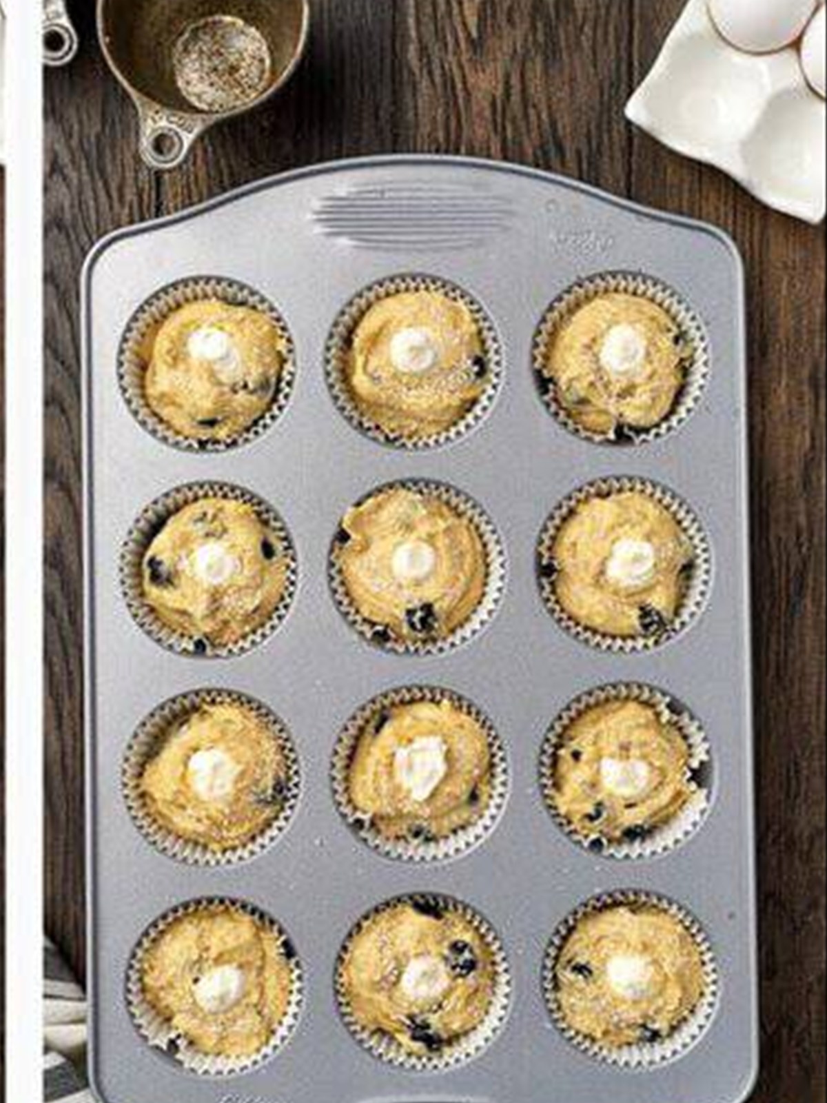 Cream cheese filling piped into the center of each blueberry muffin in the tin.