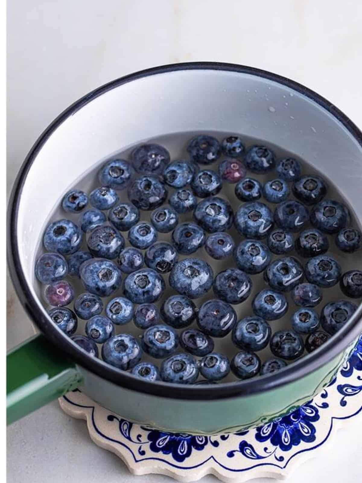 Fresh blueberries added to the simple syrup in a saucepan for Blueberry Syrup.
