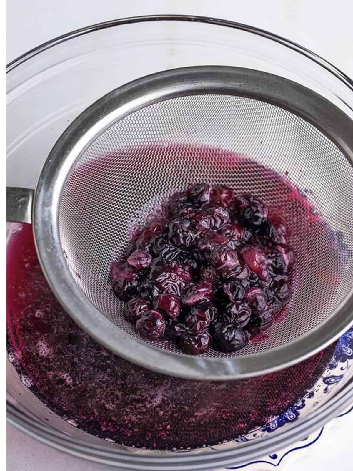 Blueberry Syrup strained through a fine mesh strainer into a glass bowl.
