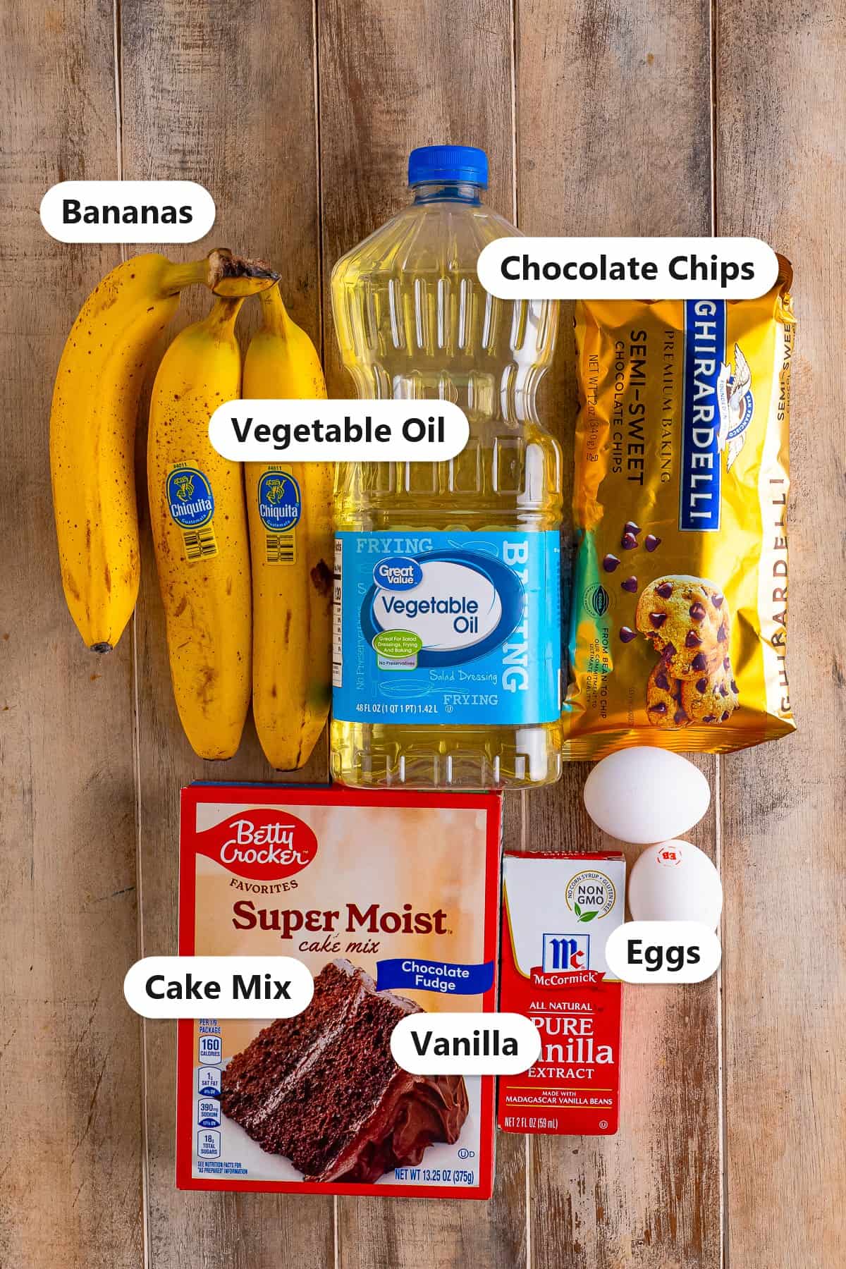 Banana Chocolate Chip Muffins ingredients including bananas, vegetable oil, chocolate chips, chocolate cake mix, eggs, and vanilla labeled on a wood board.