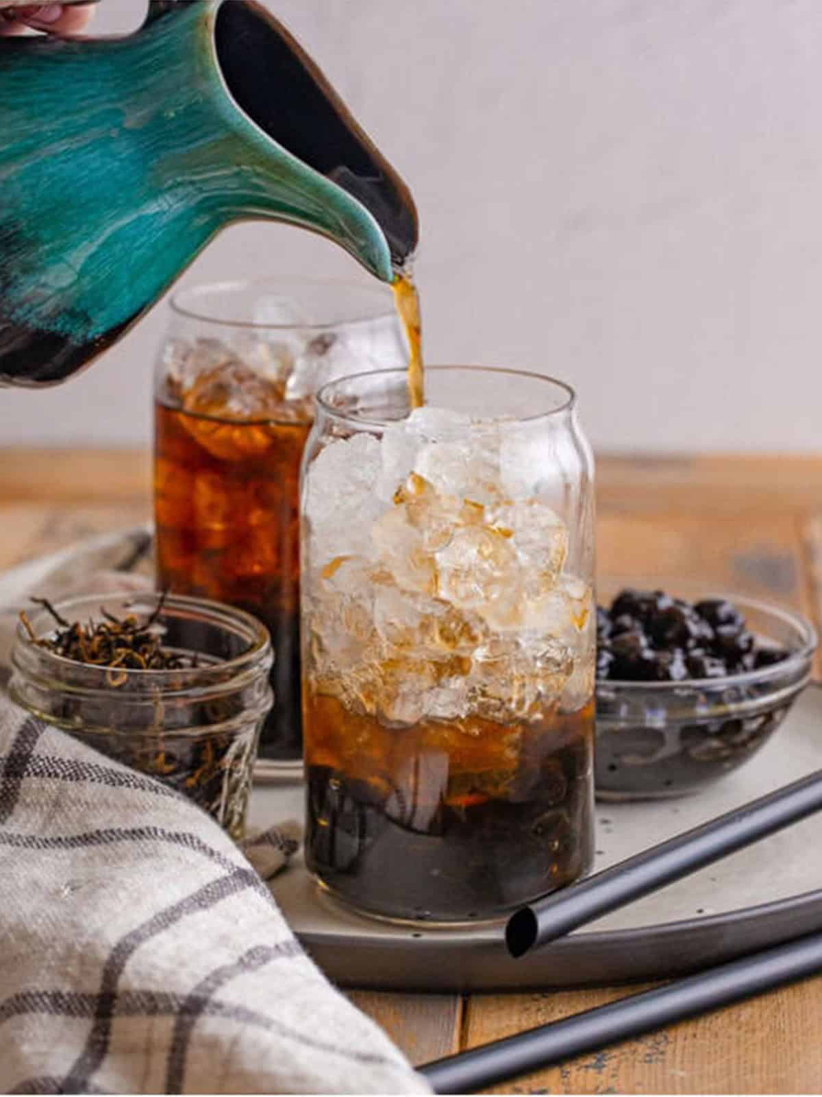 Pouring chilled tea over ice and tapioca pearls in a tall glass
