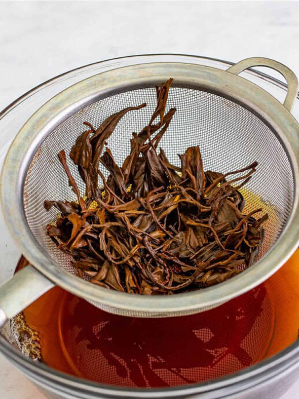 Black tea steeping and being strained through a fine mesh strainer for boba tea