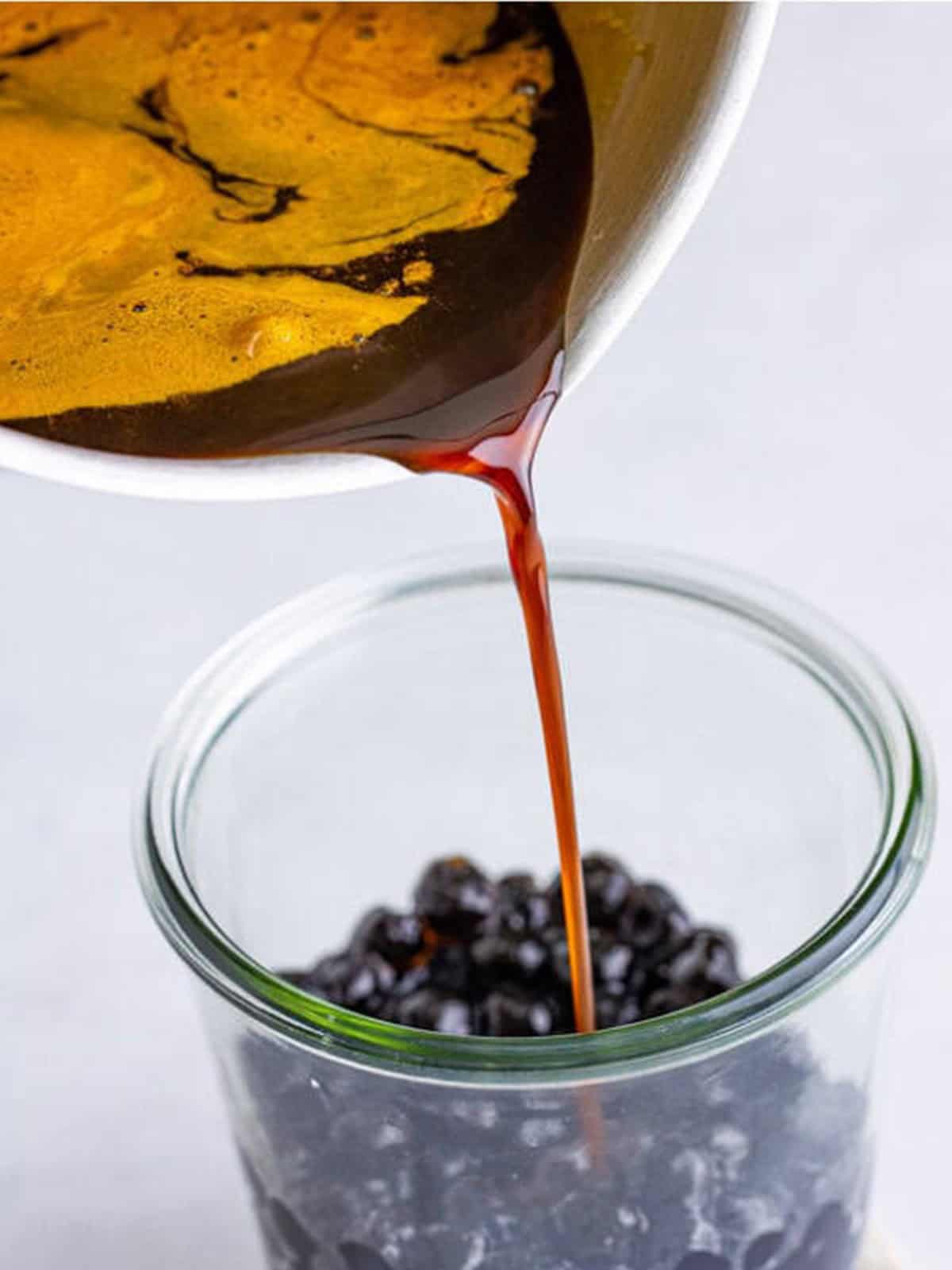 Pouring brown sugar syrup over cooked tapioca pearls in a glass
