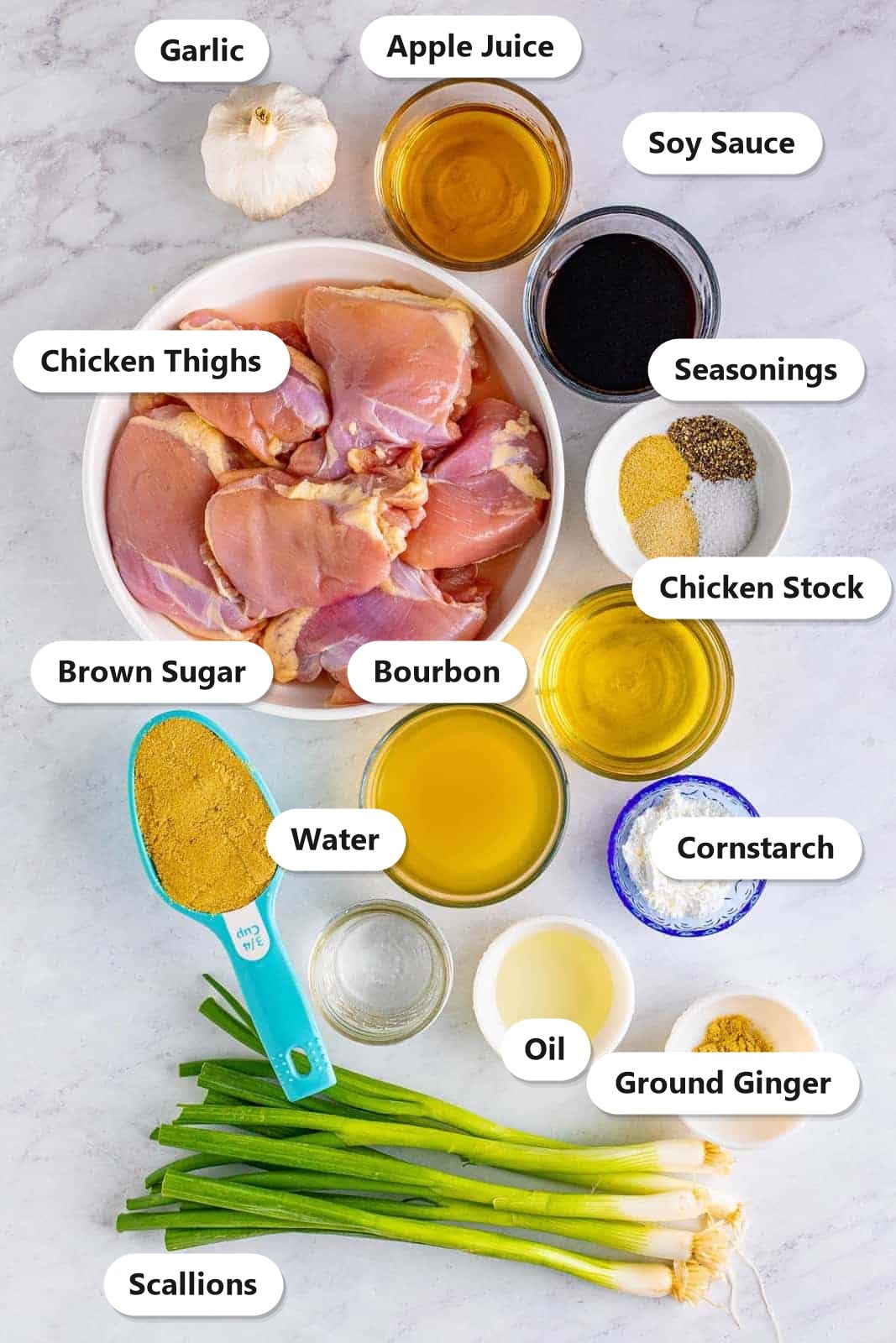 Labeled bourbon chicken ingredients including chicken thighs, bourbon, soy sauce, apple juice, brown sugar, ginger, and scallions on a marble counter.