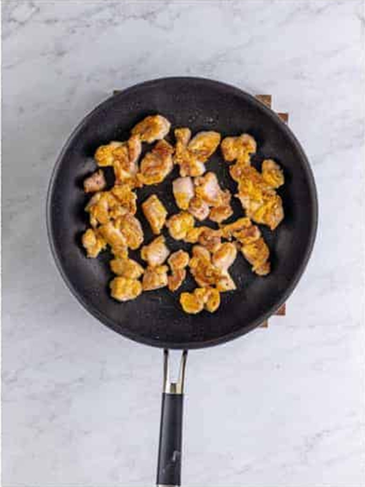 Chicken pieces seared until cooked through in a skillet for bourbon chicken.