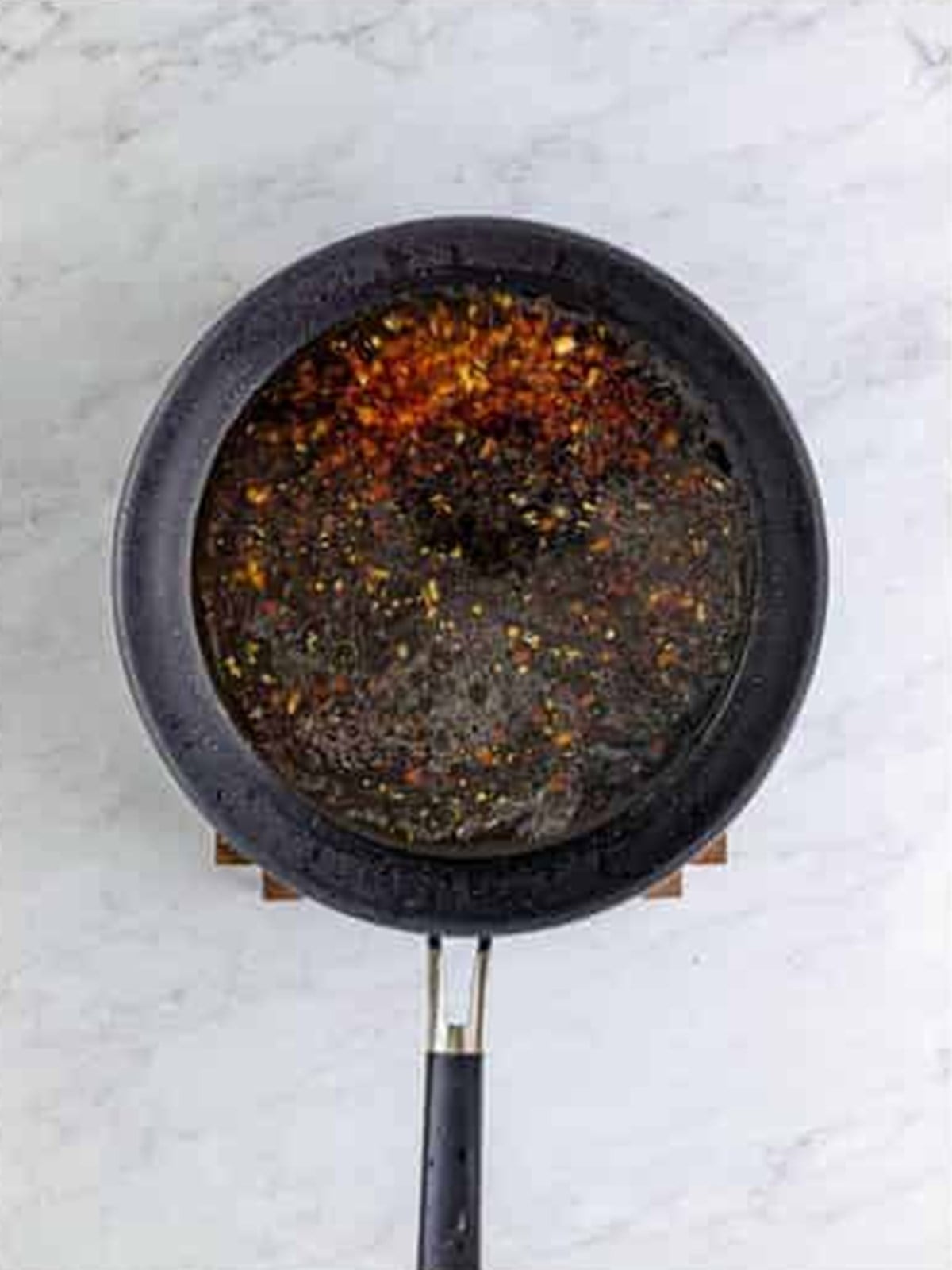 Garlic, apple juice, bourbon, and soy sauce simmering in a skillet for bourbon chicken sauce.