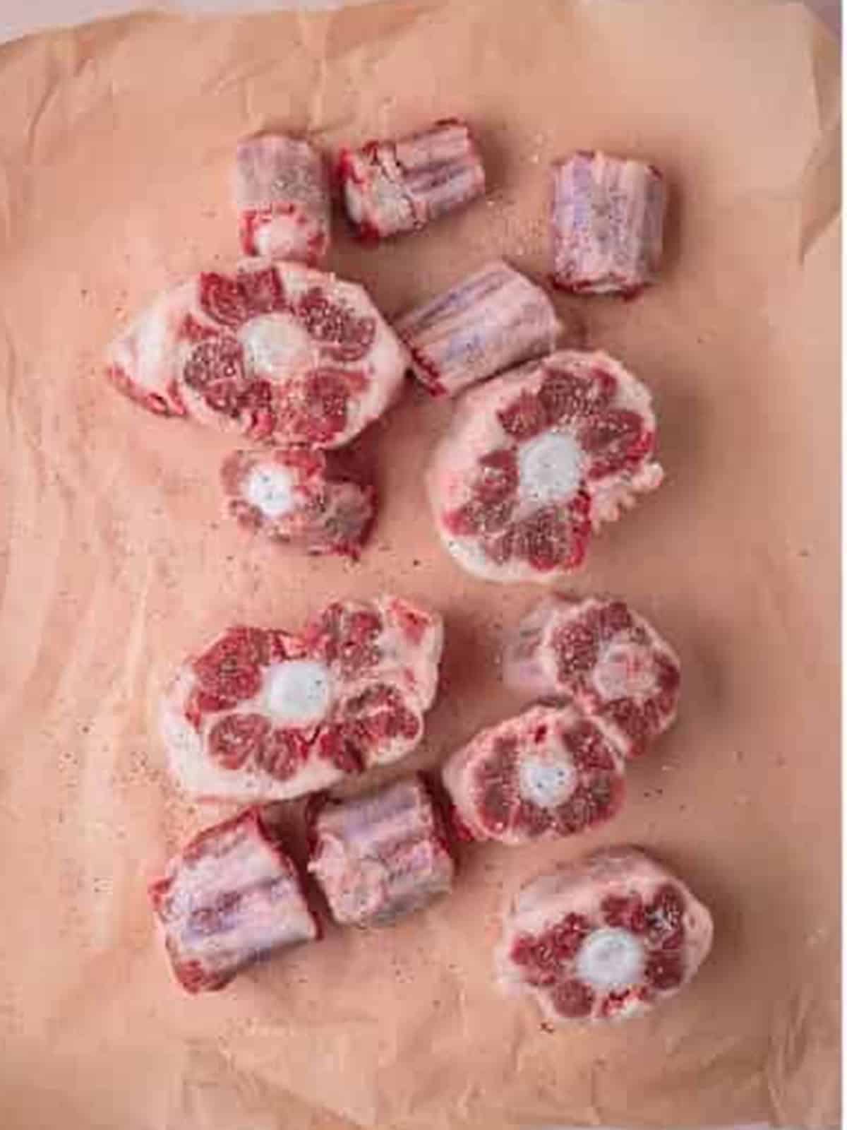 Raw beef oxtails trimmed and seasoned with salt and pepper on parchment paper.