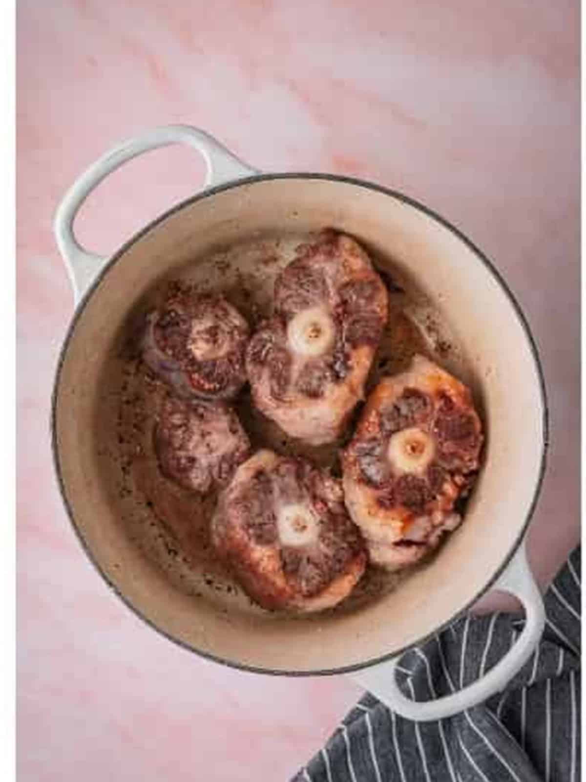 Oxtails browned on all sides in a white Dutch oven.
