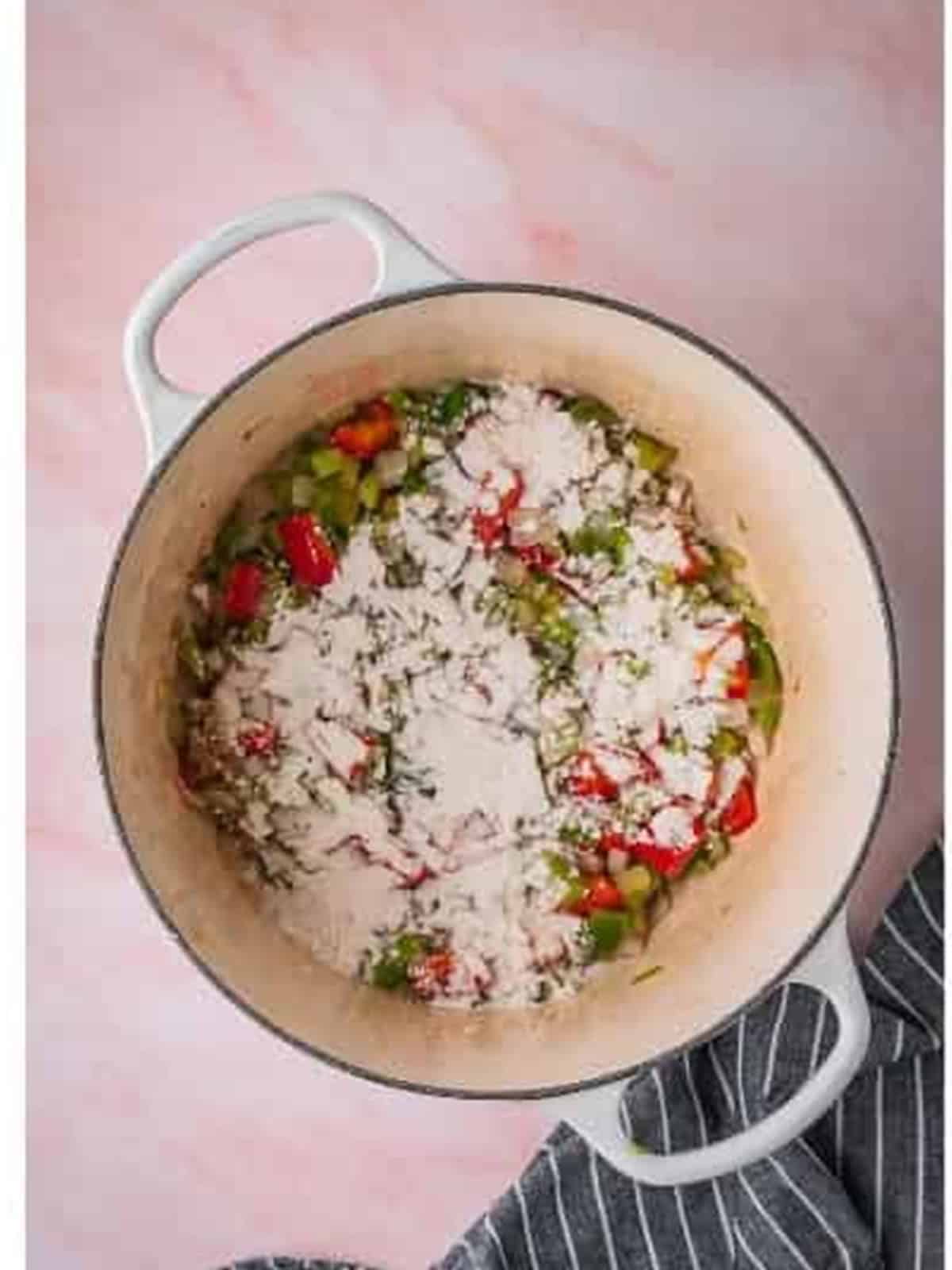 Flour sprinkled over sauteed vegetables in a Dutch oven.