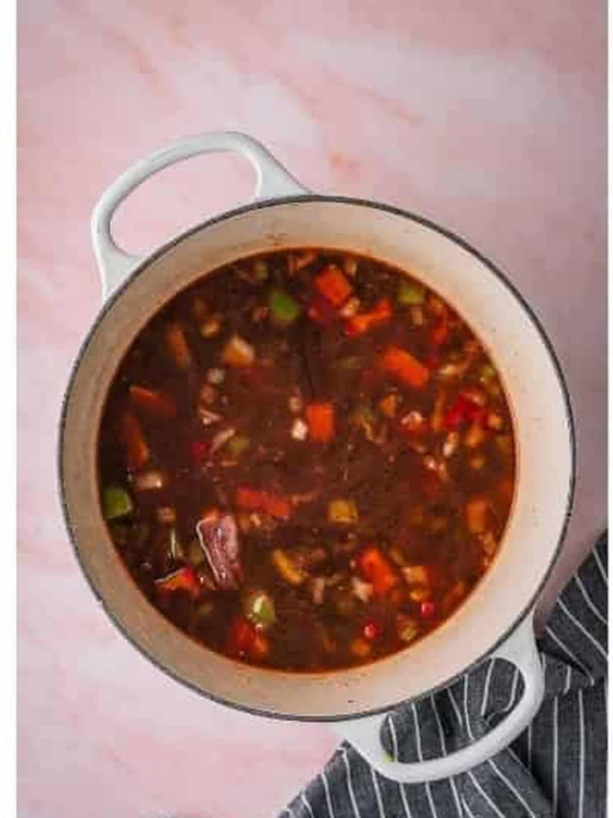 Oxtails returned to a dark braising liquid with herbs and seasonings in a Dutch oven.
