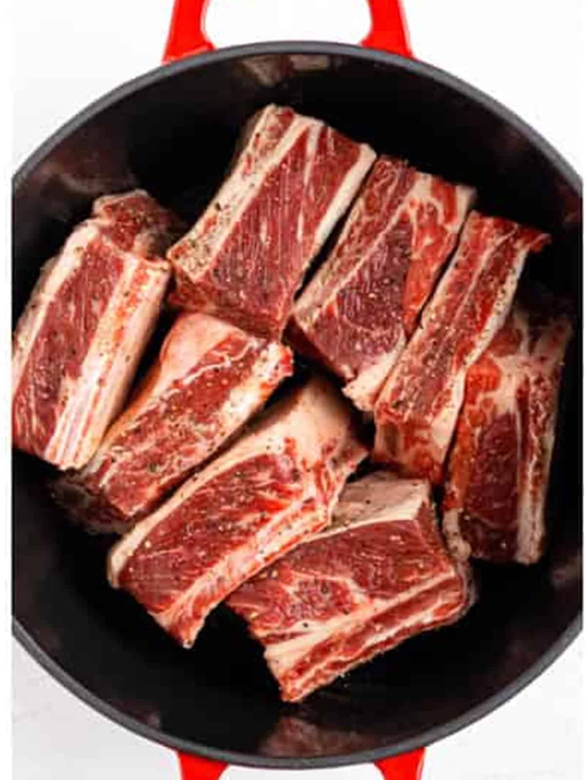 Raw bone in beef short ribs seasoned with salt and pepper in a Dutch oven.