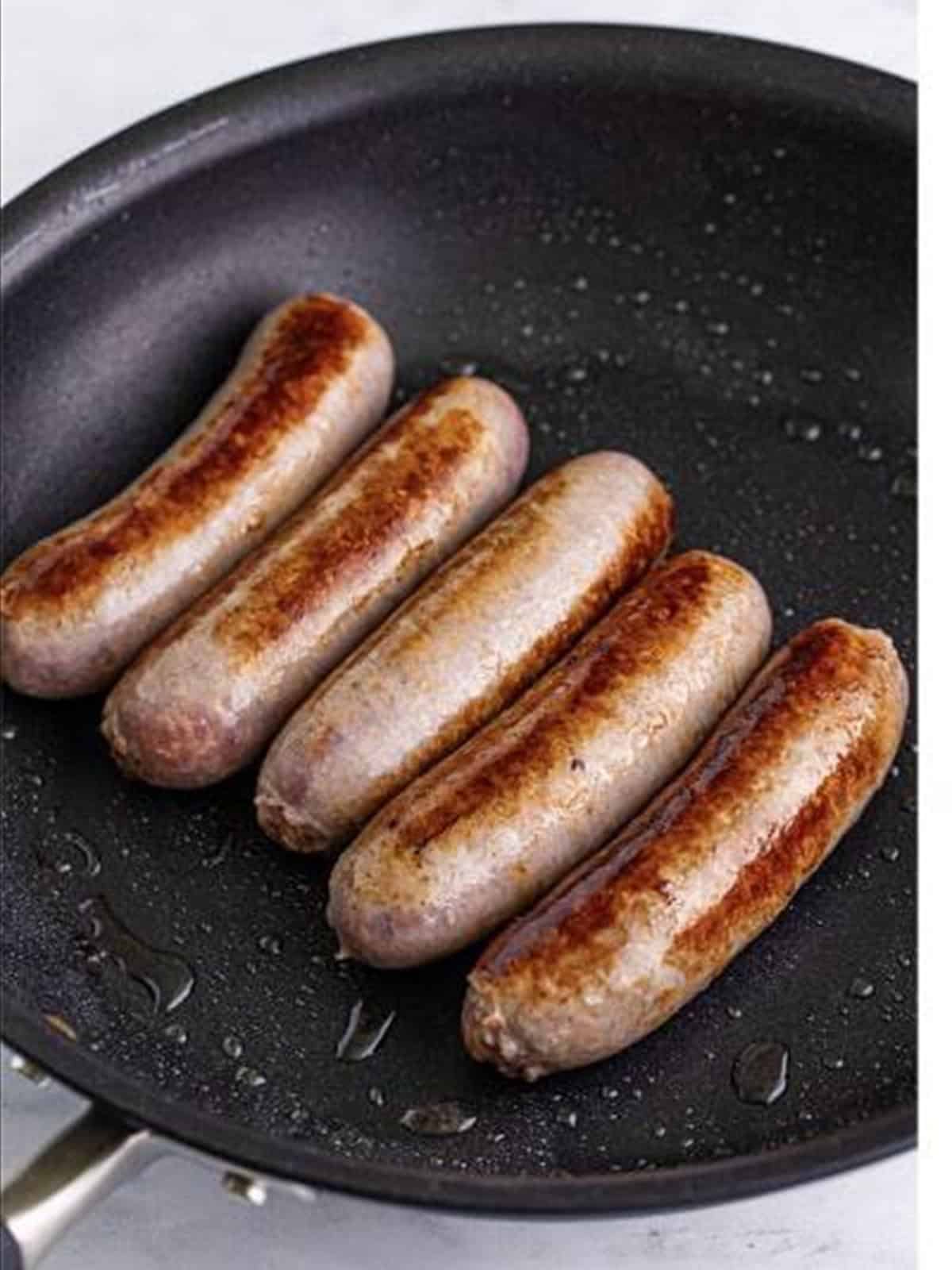 Browning bratwurst in a skillet for brats and sauerkraut.