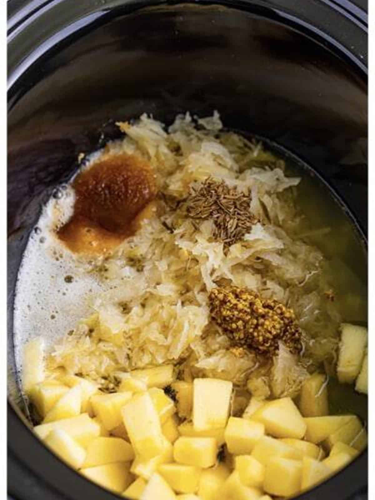 Sauerkraut, apple, and seasonings in the slow cooker for brats and sauerkraut.