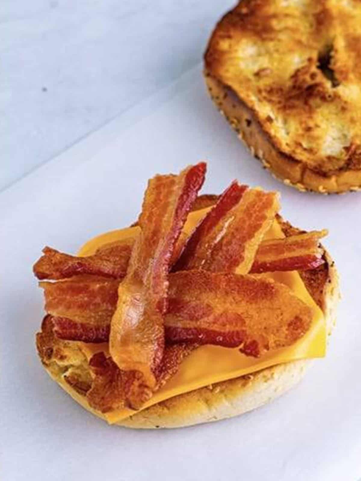 Crispy bacon strips stacked on the cheesy bottom half of the bagel.