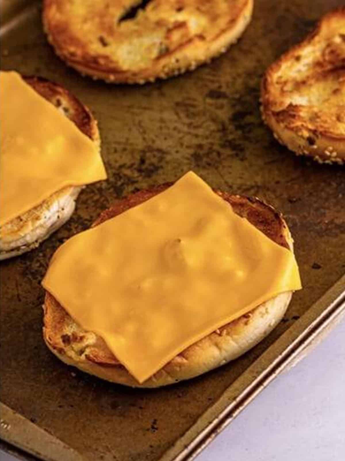 A slice of American cheese placed on the toasted bottom half of an everything bagel.