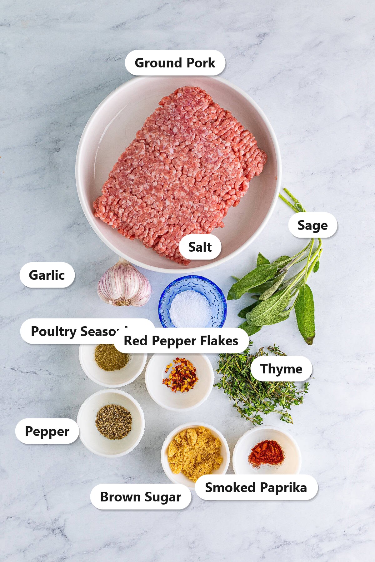 Labeled breakfast sausage ingredients including ground pork, garlic, brown sugar, sage, thyme, and spices on a marble counter.