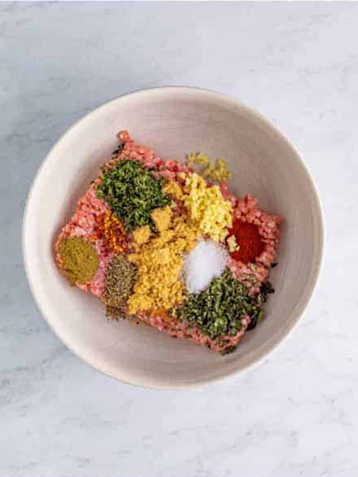 Ground pork with garlic, brown sugar, herbs, and spices in a bowl for breakfast sausage.
