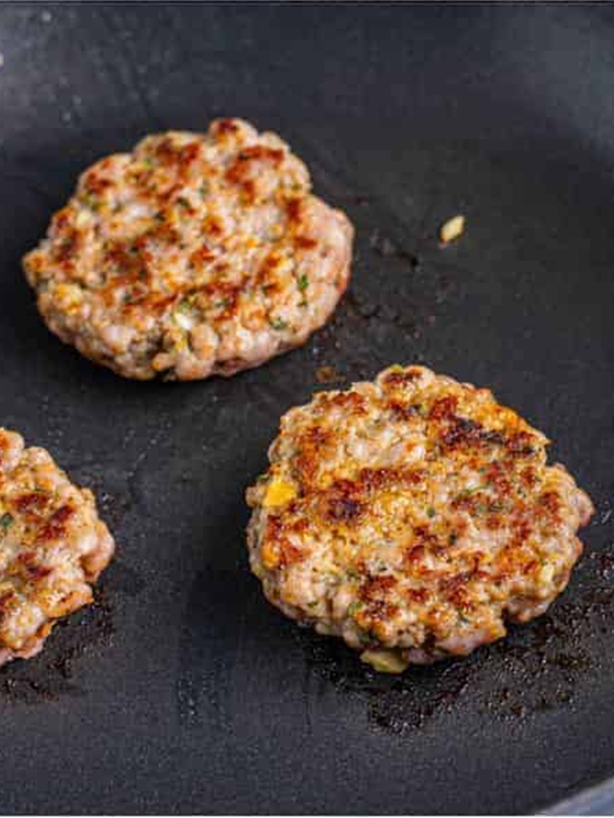 Breakfast sausage patties browning in a skillet until cooked through.