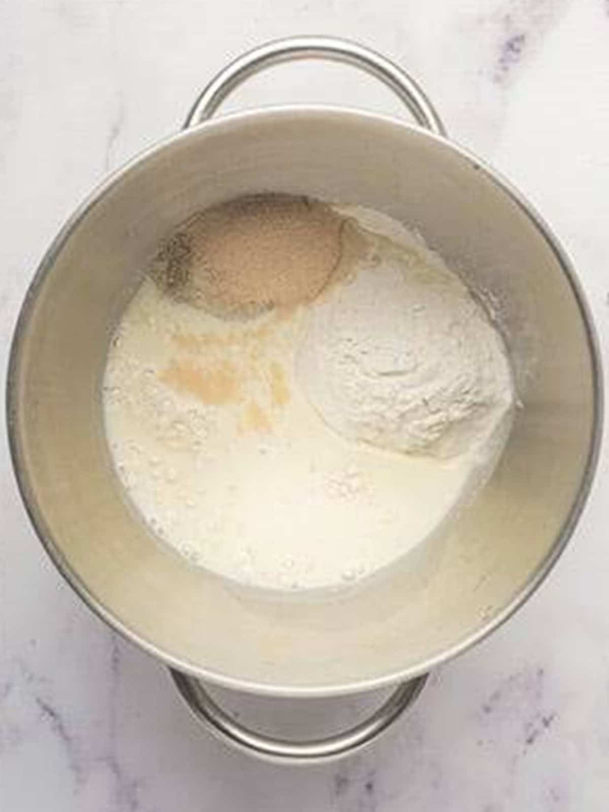 Yeast, flour, sugar, and warm milk combined into a paste in a stand mixer bowl for brioche bread.