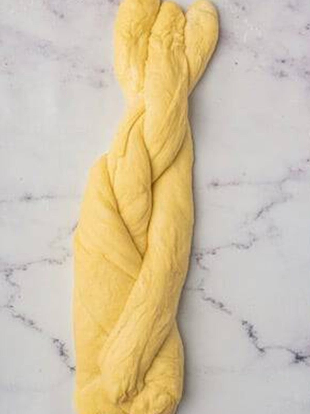 Three ropes of brioche dough braided together into a loaf.