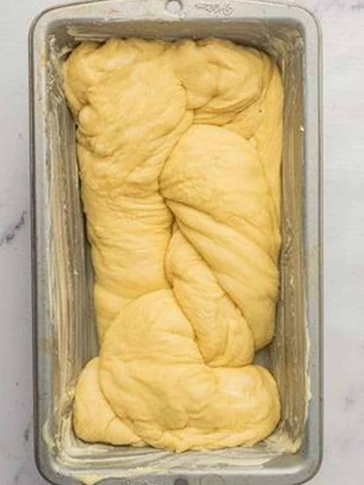 A braided brioche loaf placed into a greased loaf pan to rise.