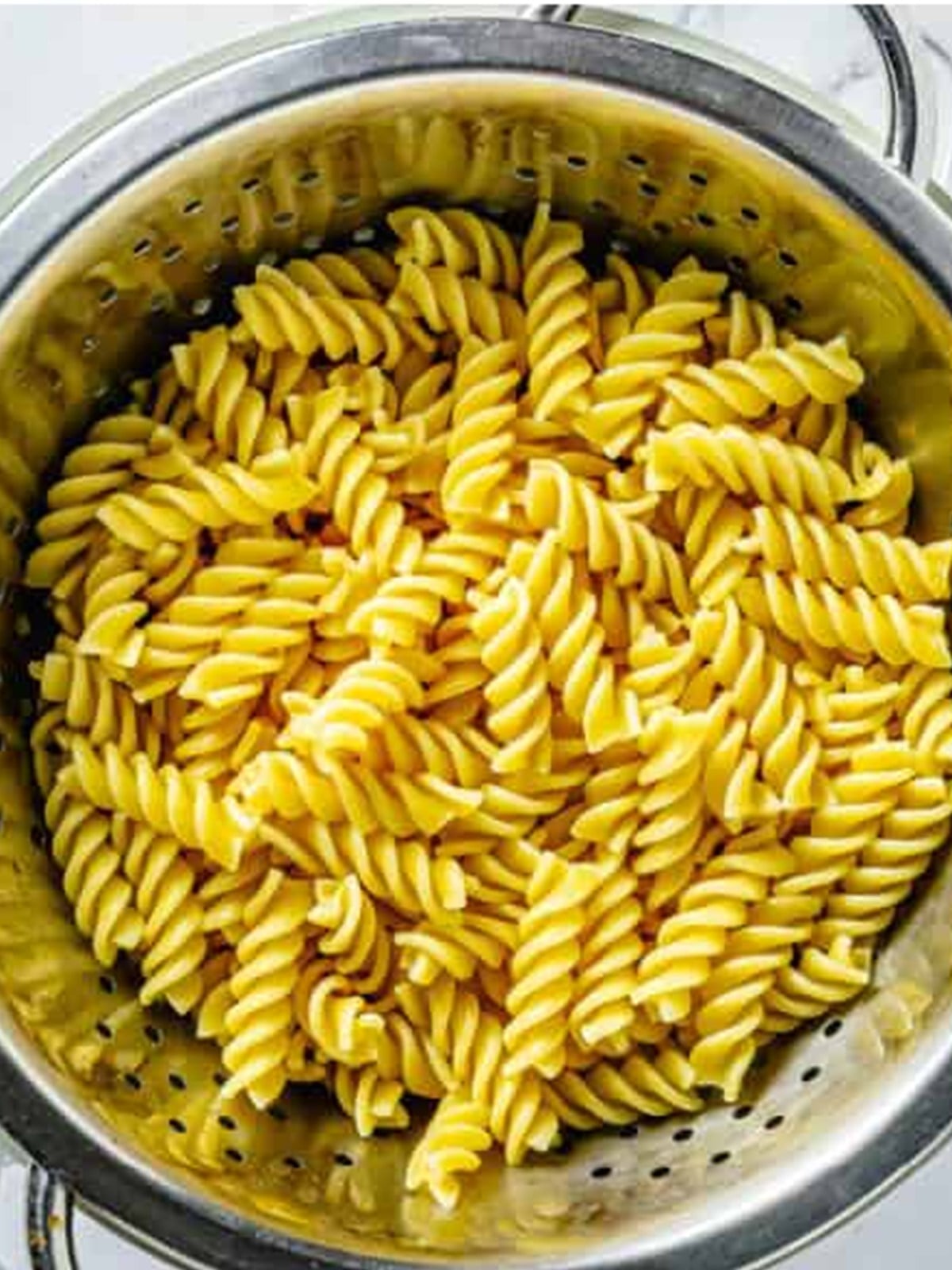 Cooked rotini pasta draining in a colander for broccoli pasta salad.