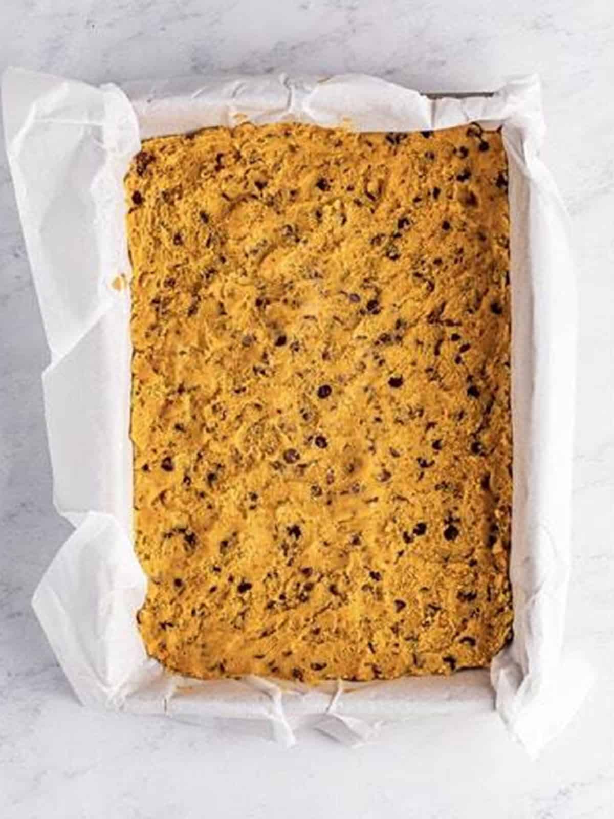 Chocolate chip cookie dough pressed into a parchment lined pan for Brookies.