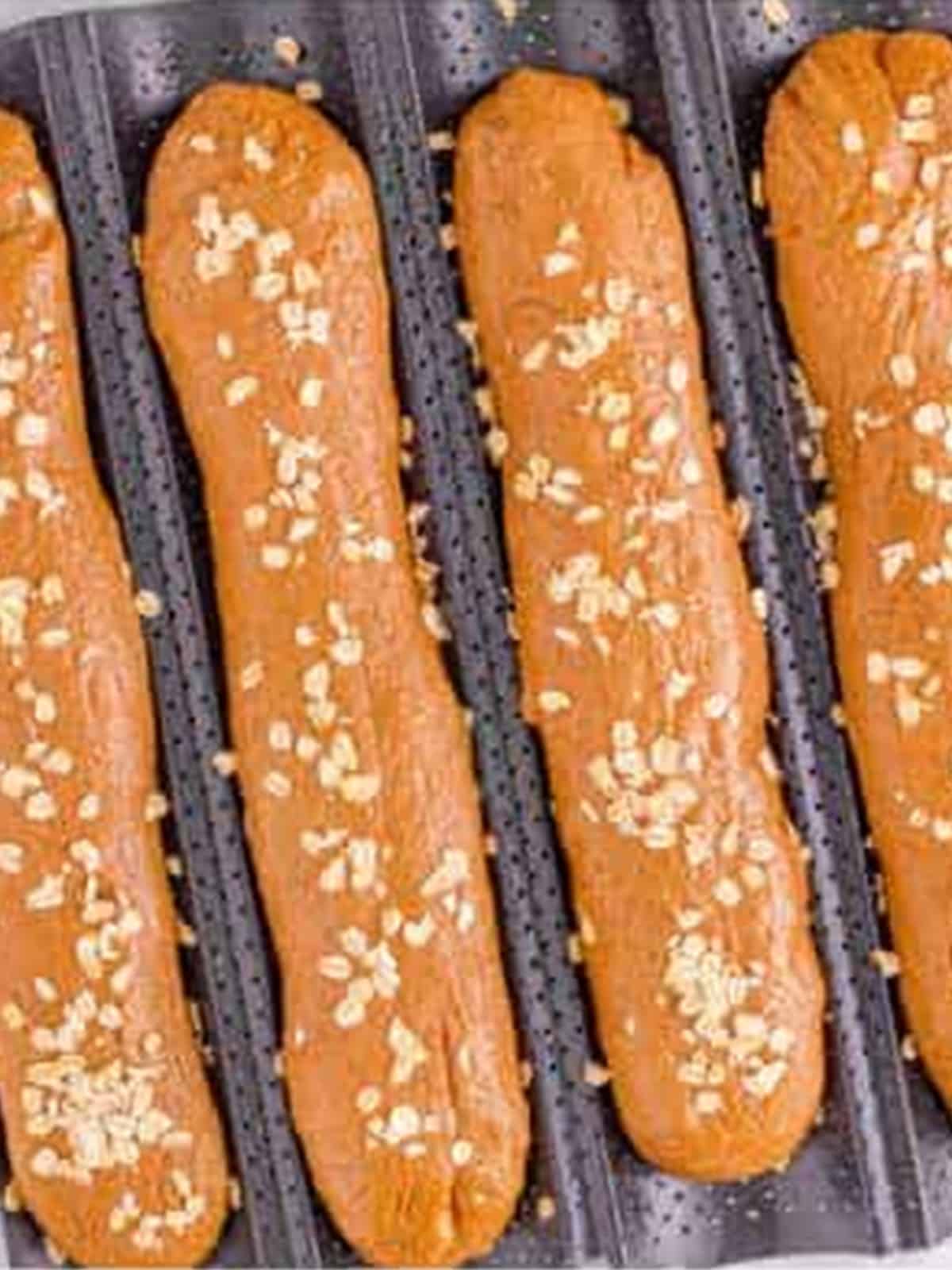 Shaped brown bread baguettes dusted with oats on a perforated baguette pan.